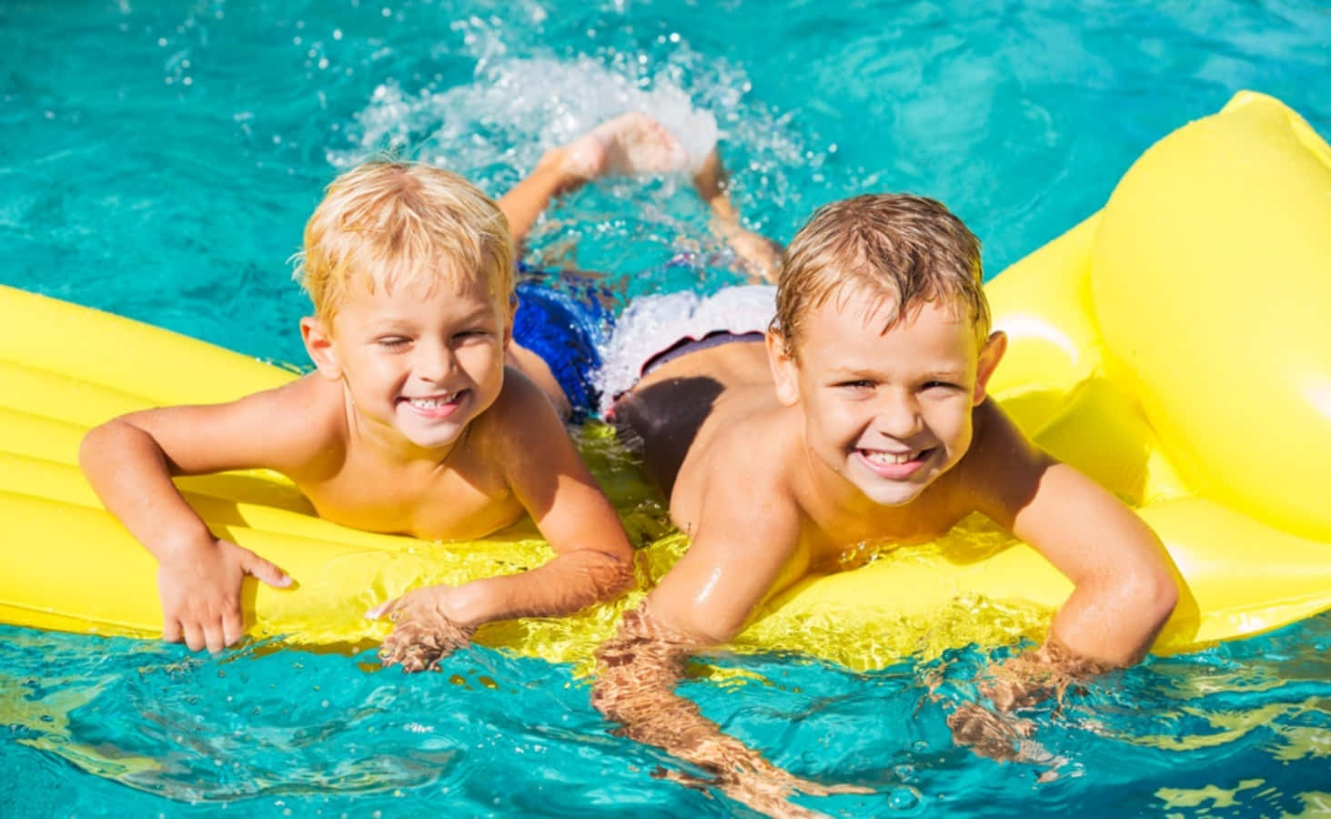 Swimming 桌布 壁紙 — 兩個快樂的男孩在閃閃發光的藍色游泳池中騎著黃色充氣筏，對著鏡頭咧嘴笑。