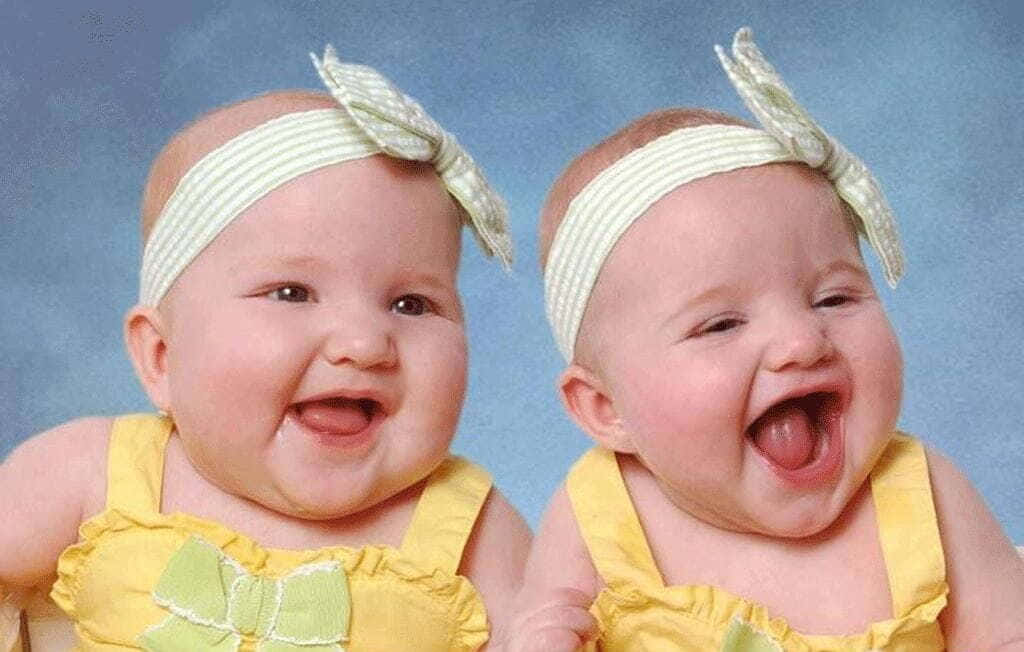 Cute Babies 桌布 壁紙 — 兩個快樂的雙胞胎嬰兒穿著黃色連衣裙和綠色蝴蝶結，在柔和的藍色工作室背景下開懷大笑。
