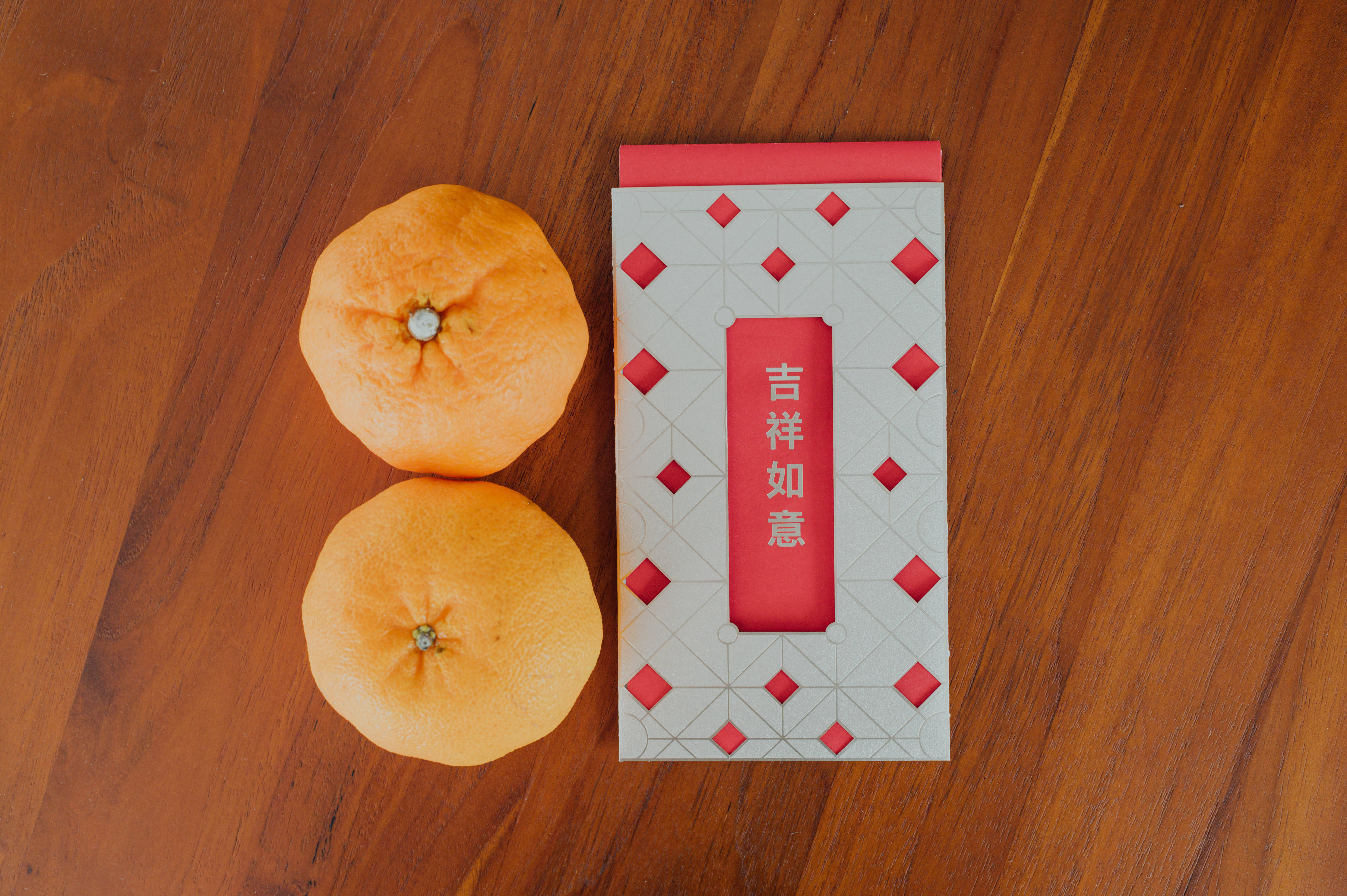 New 桌布 壁紙 — 兩個成熟的柳橙旁邊放著一個帶有中文字的紅白圖案信封，放在溫暖的木質表面上。