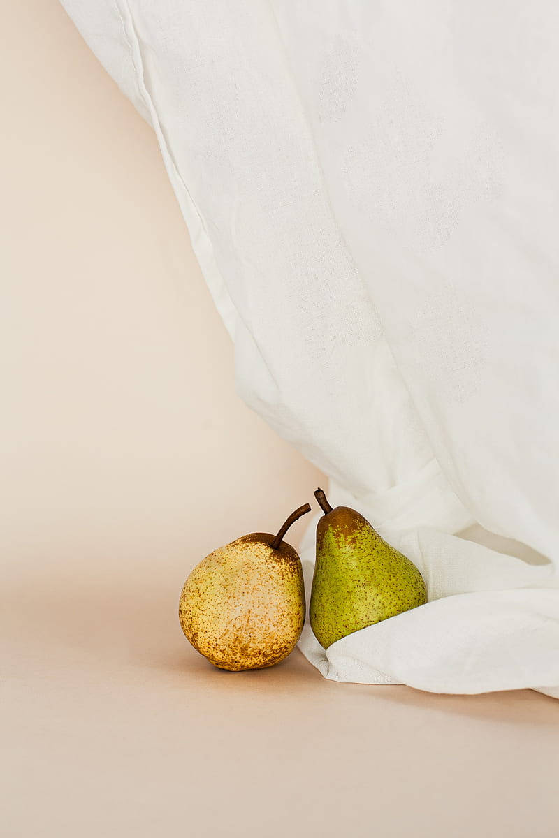 Fruits 桌布 壁紙 — 兩個成熟的梨子放在柔軟的米色表面上，旁邊是垂墜的白色布料，構成極簡風格的靜物畫。