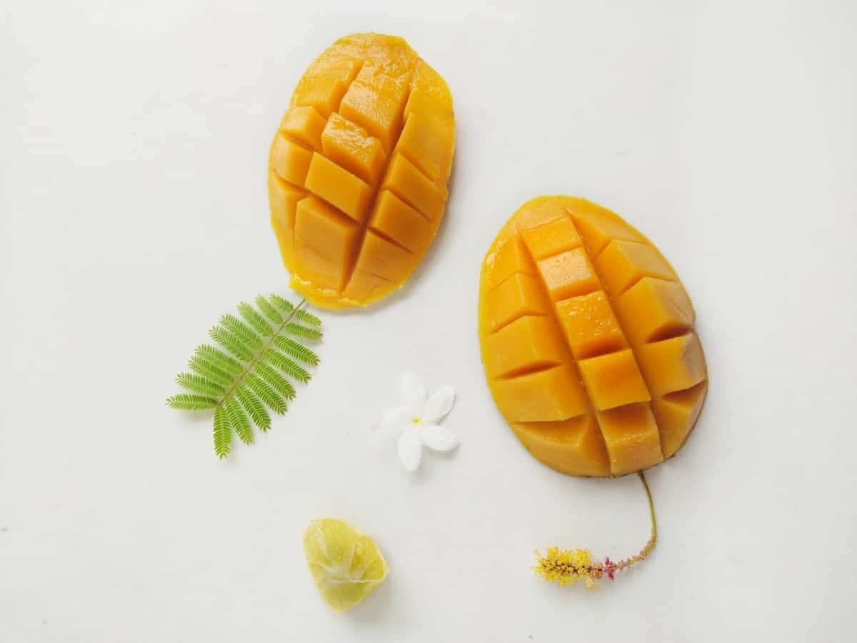 Mango 桌布 壁紙 — 兩個成熟的芒果切成方塊，放在白色表面上，旁邊有蕨葉和小白花。