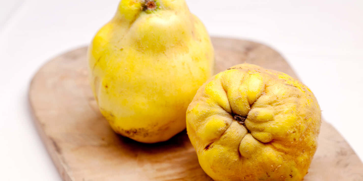 Quince 桌布 壁紙 — 兩個成熟的黃色榲桲，表皮帶有紋理，放在淺色木砧板上，背景是明亮的白色。