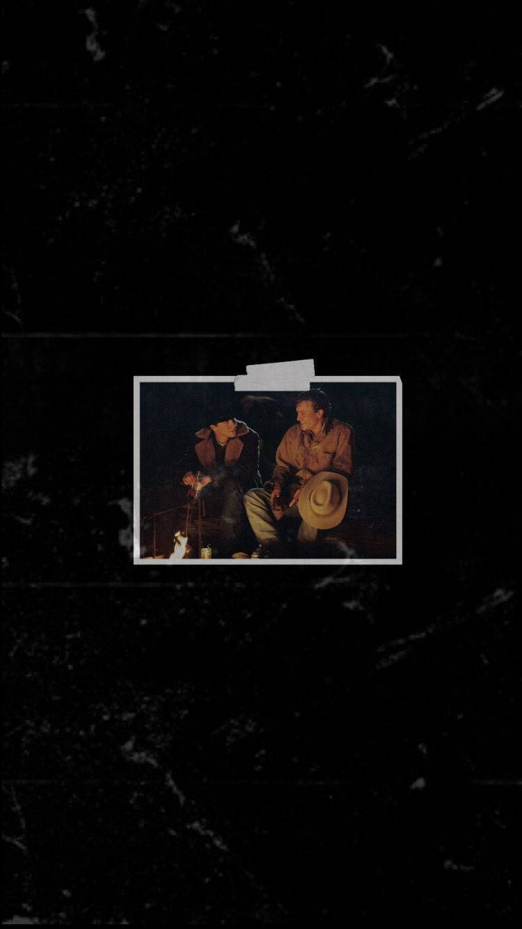 brokeback mountain 桌布 壁紙 — 兩個戴牛仔帽的男人坐在一個昏暗的相框裡，相框用膠帶貼在裂開的黑色牆壁上，共享寧靜時刻。
