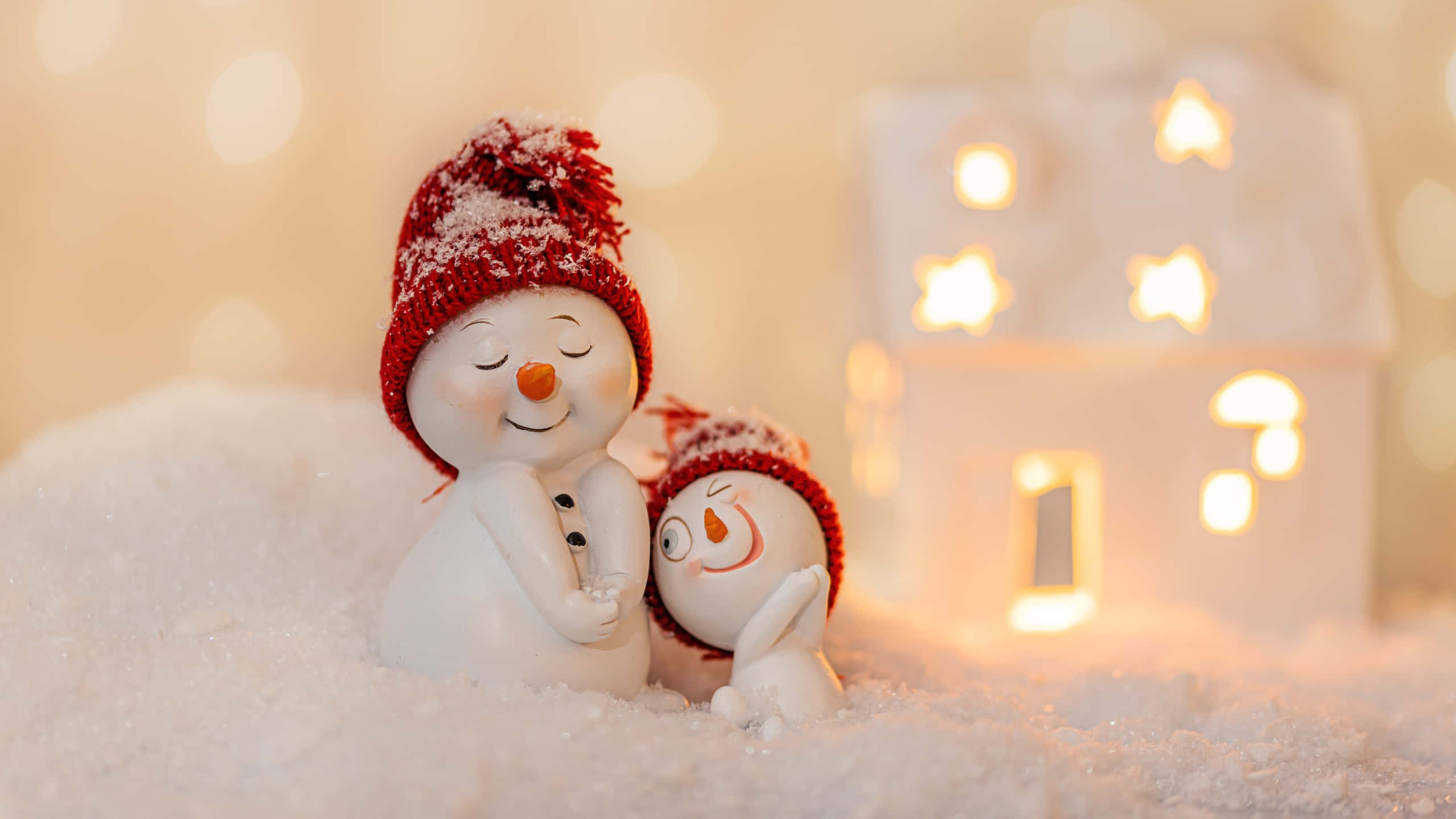 可愛聖誕節 桌布 壁紙 — 兩個戴紅帽的雪人公仔在白雪皚皚的前景中依偎，旁邊是一座閃爍星光的房子。