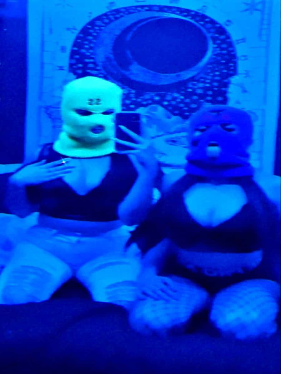 Ski Mask Girl 桌布 壁紙 — 兩個戴著全臉面具的人物在藍色紫外光下，以圖案牆為背景自拍。