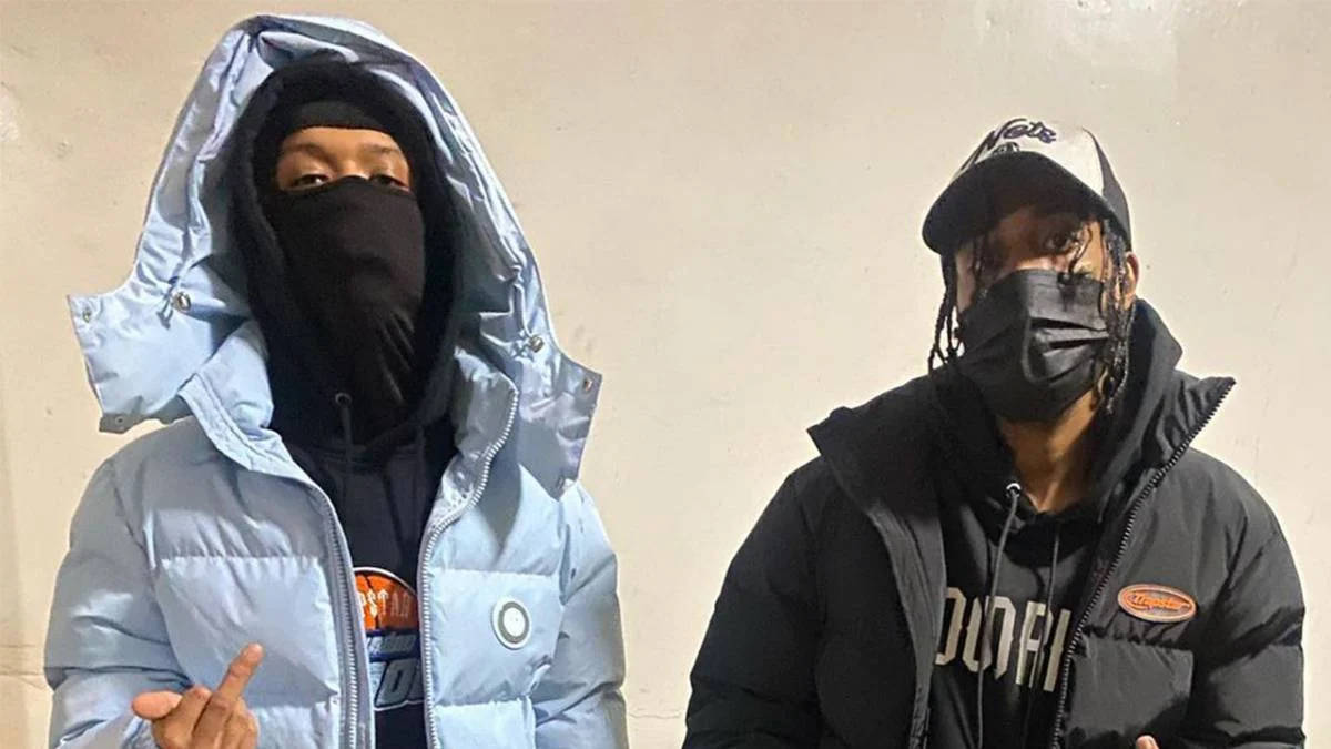 嘻哈 桌布 壁紙 — 兩個戴著口罩的人穿著羽絨外套，在素色牆前擺姿勢，一個穿淺藍色連帽衫，另一個戴黑色帽子和穿黑色外套。