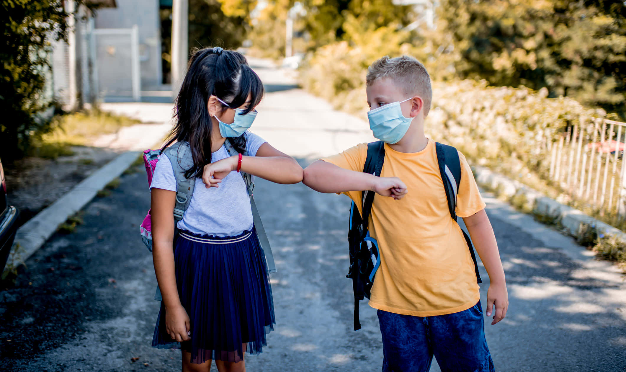 children 桌布 壁紙 — 兩個戴著口罩的小孩在陽光明媚的郊區街道上友好地互相碰肘。
