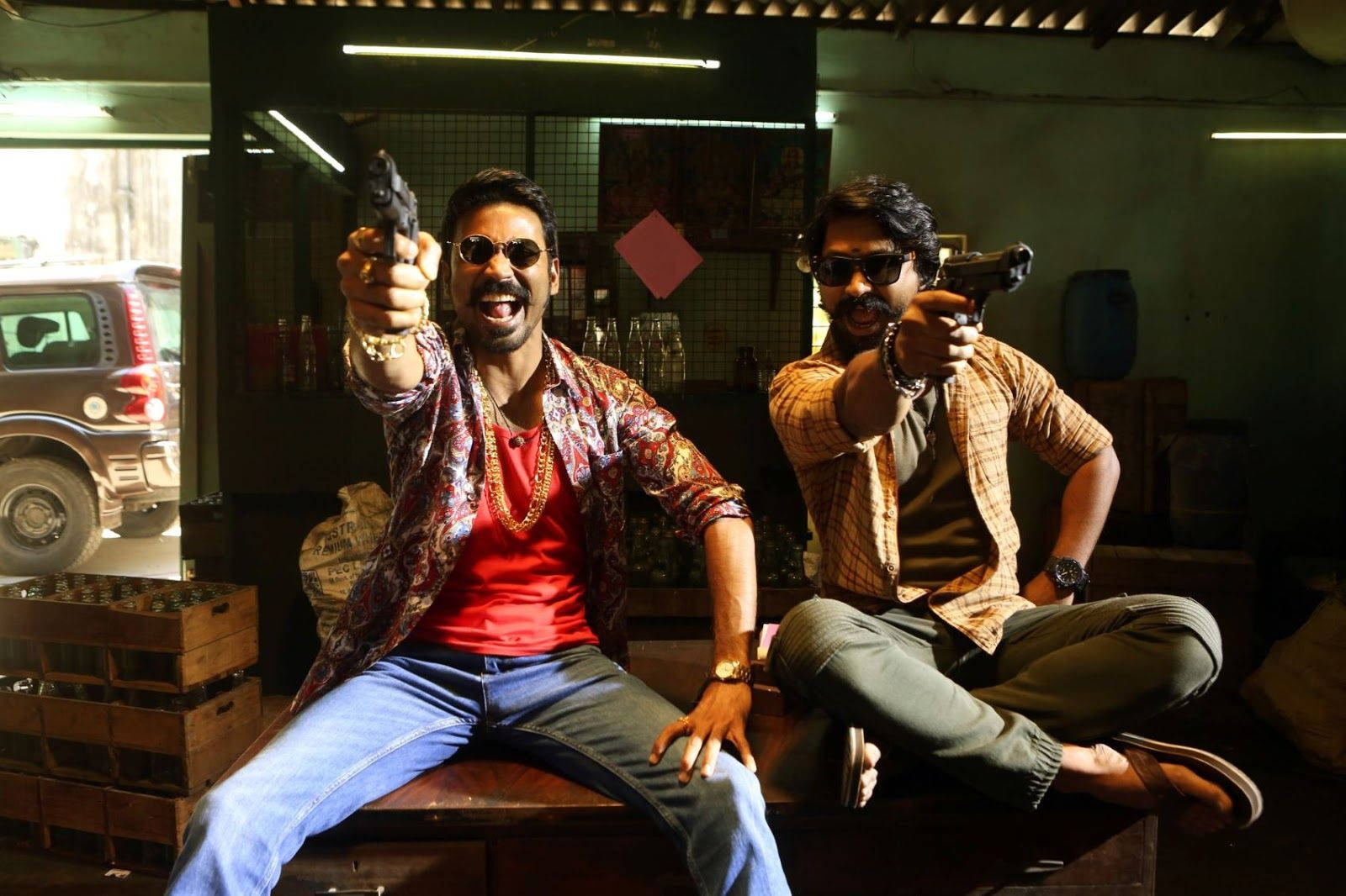 Dhanush 桌布 壁紙 — 兩個戴著太陽眼鏡的男人在雜亂昏暗的車庫裡，帶著兇猛的笑容瞄準手槍。
