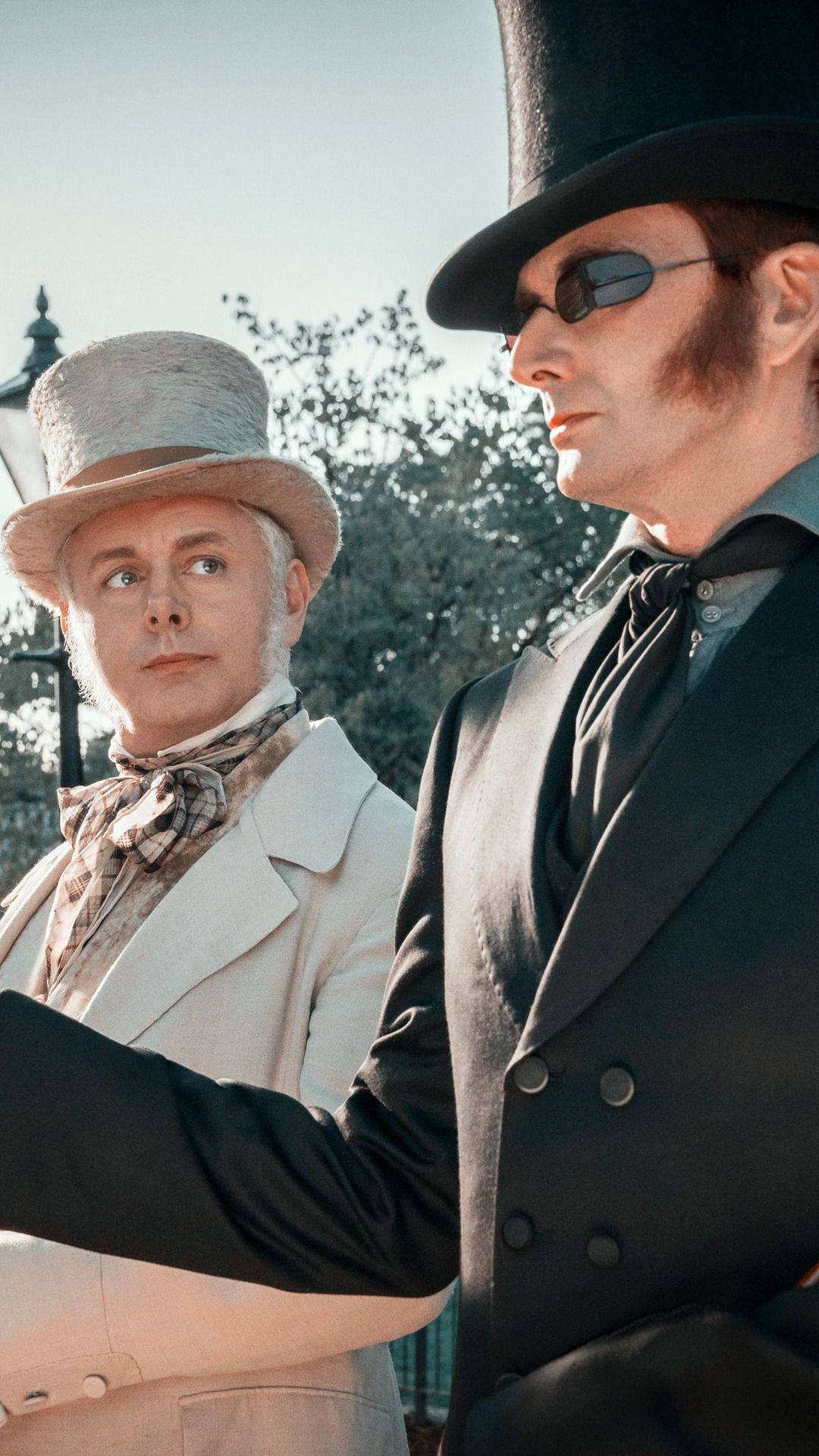 Good Omens 桌布 壁紙 — 兩個戴著復古高帽的男人，其中一個戴著太陽眼鏡，並排站在陽光普照的戶外環境中。