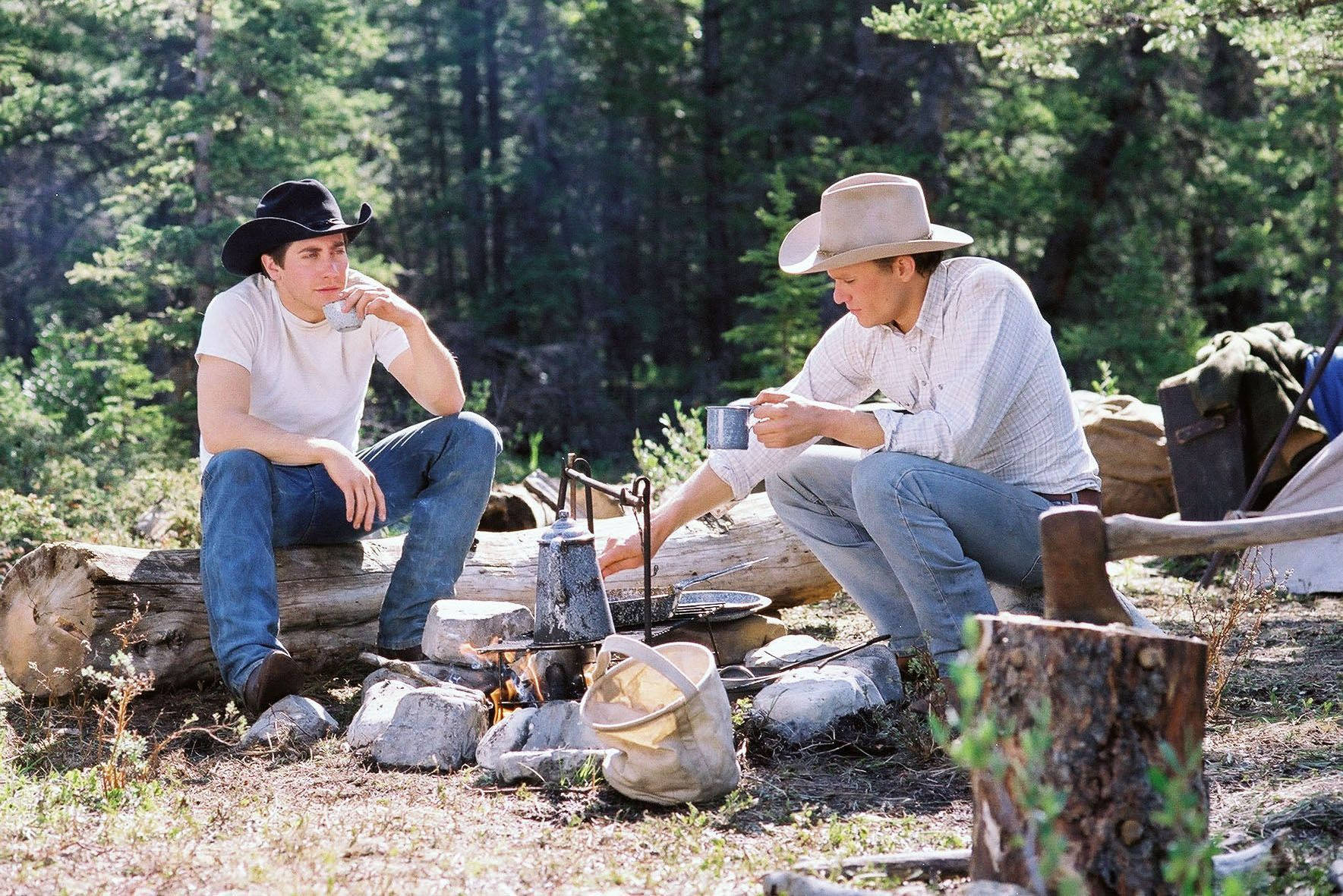 brokeback mountain 桌布 壁紙 — 兩個戴著牛仔帽的牛仔在茂密綠色森林環繞的營火旁啜飲咖啡。