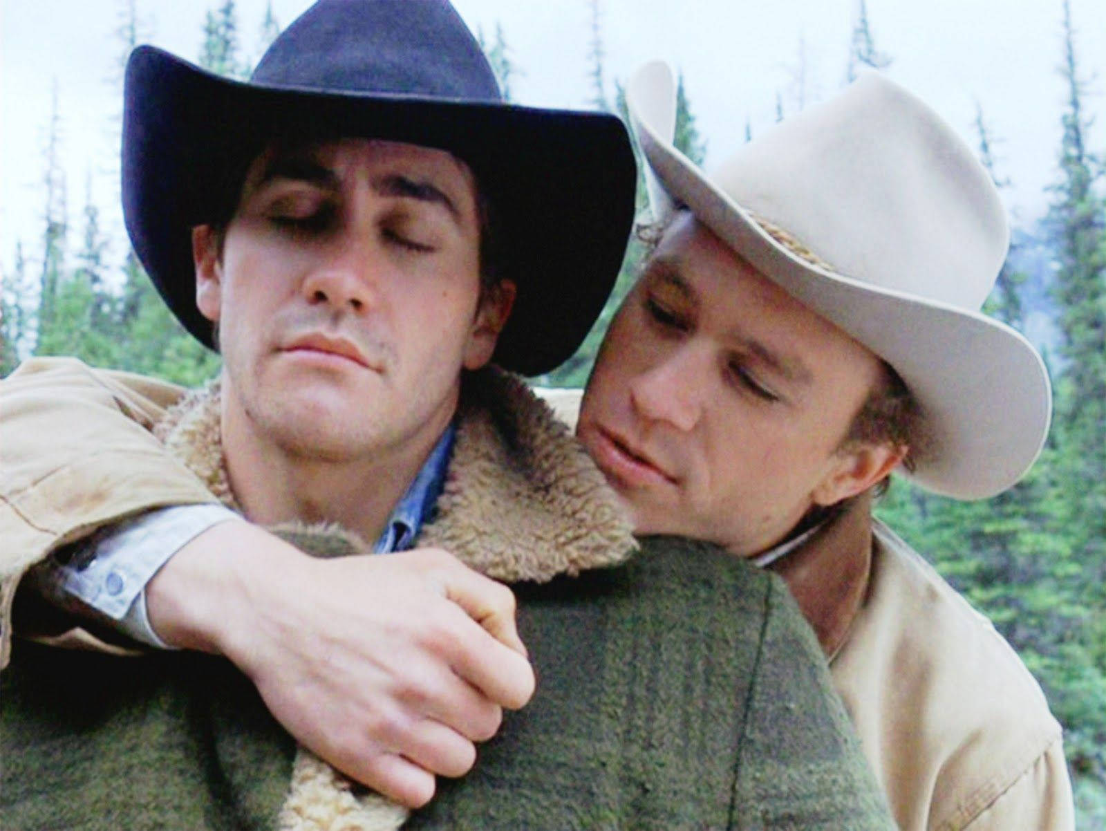 brokeback mountain 桌布 壁紙 — 兩個戴著牛仔帽的男人在身後有高大松樹的森林中溫柔擁抱。