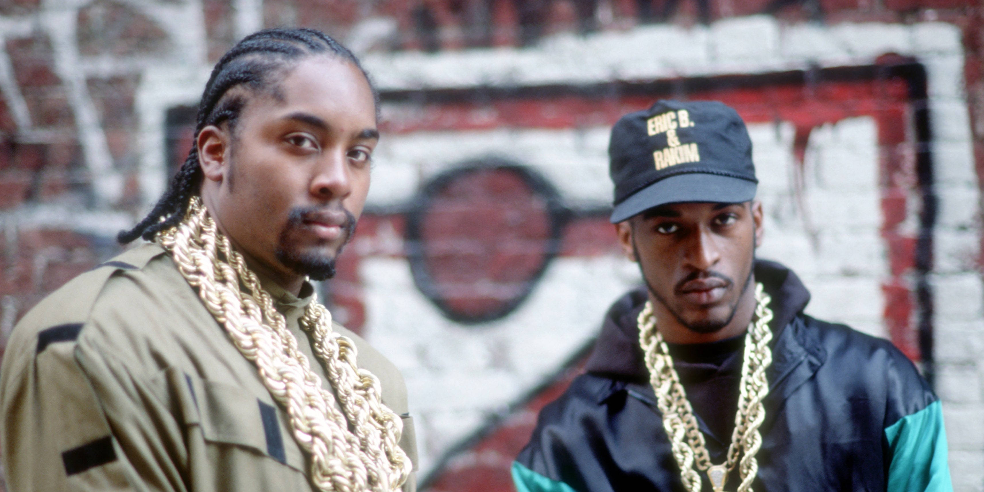 Rappers 桌布 壁紙 — 兩個戴著金鏈的男人自信地站在城市環境中佈滿塗鴉的磚牆前。