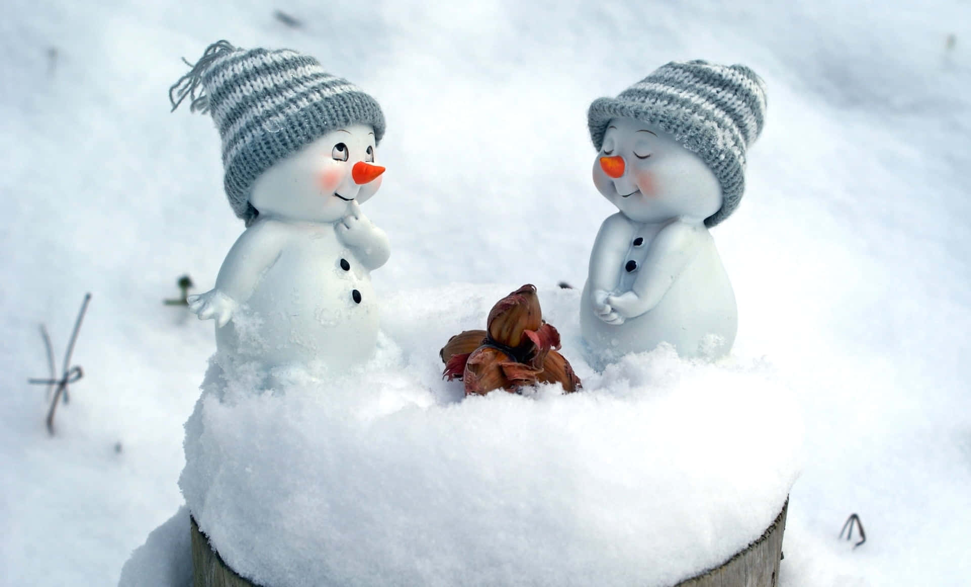可愛聖誕風格 桌布 壁紙 — 兩個戴著針織帽的可愛雪人公仔，在新雪中圍著一小堆秋葉分享溫馨時刻。
