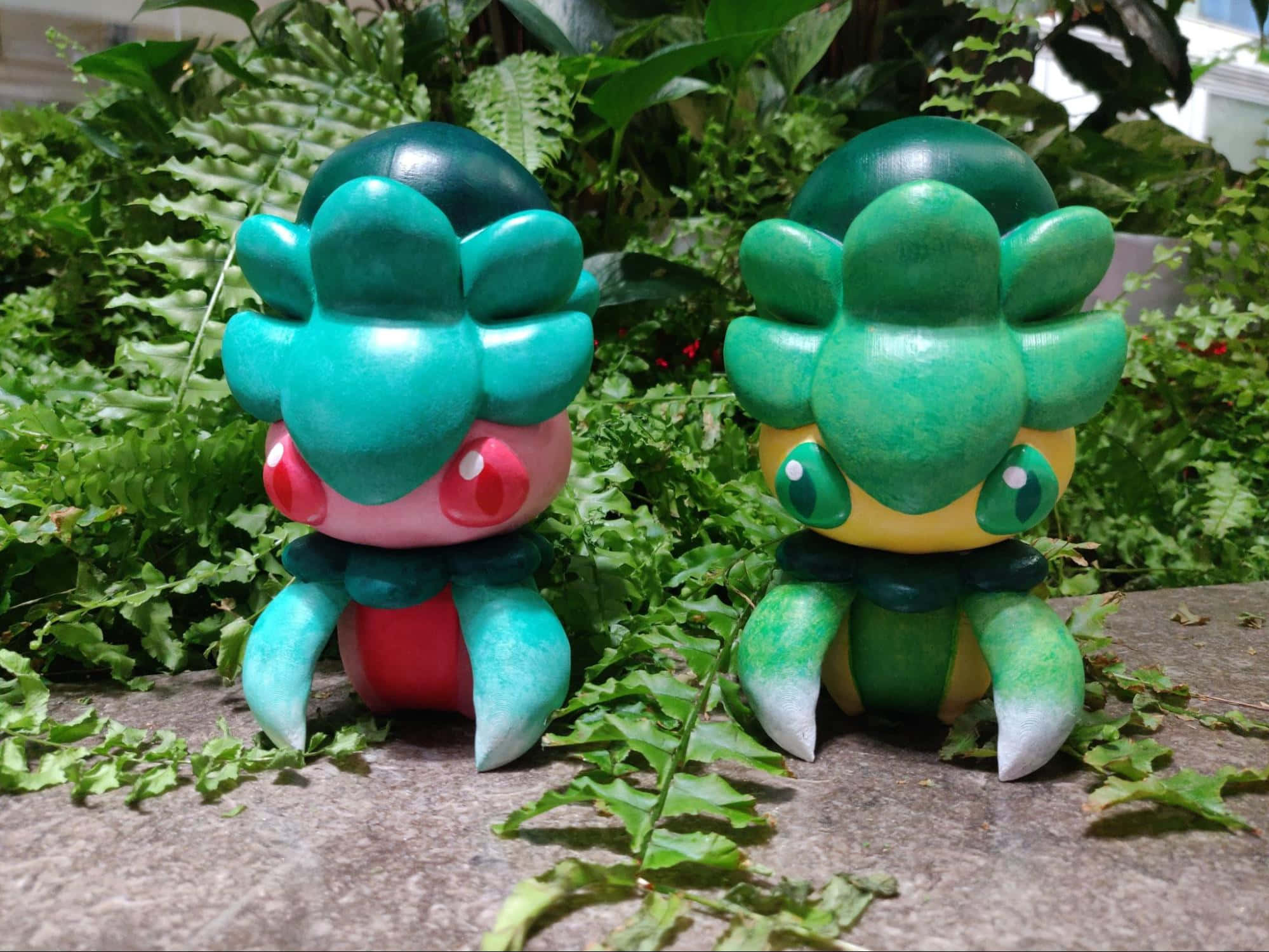 寶可夢 桌布 壁紙 — 兩個手繪的 Bulbasaur 公仔並排坐在石頭上，周圍是茂密的蕨類植物，在花園環境中。