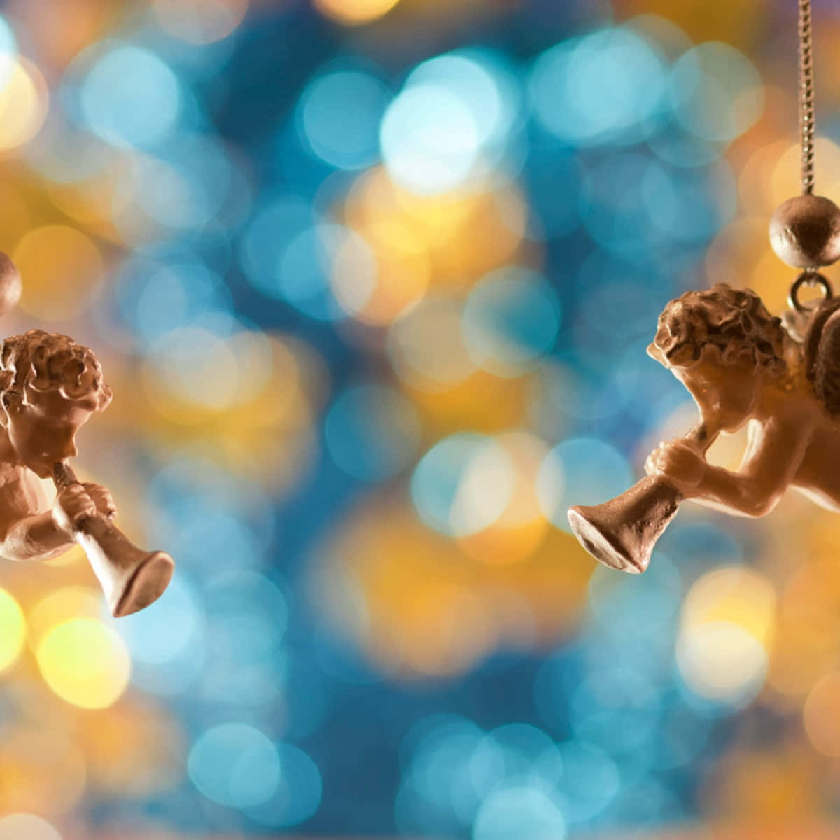 Religious Christmas 桌布 壁紙 — 兩個拿著喇叭的小天使雕像掛在藍色和金色燈光的鮮豔散景背景上。