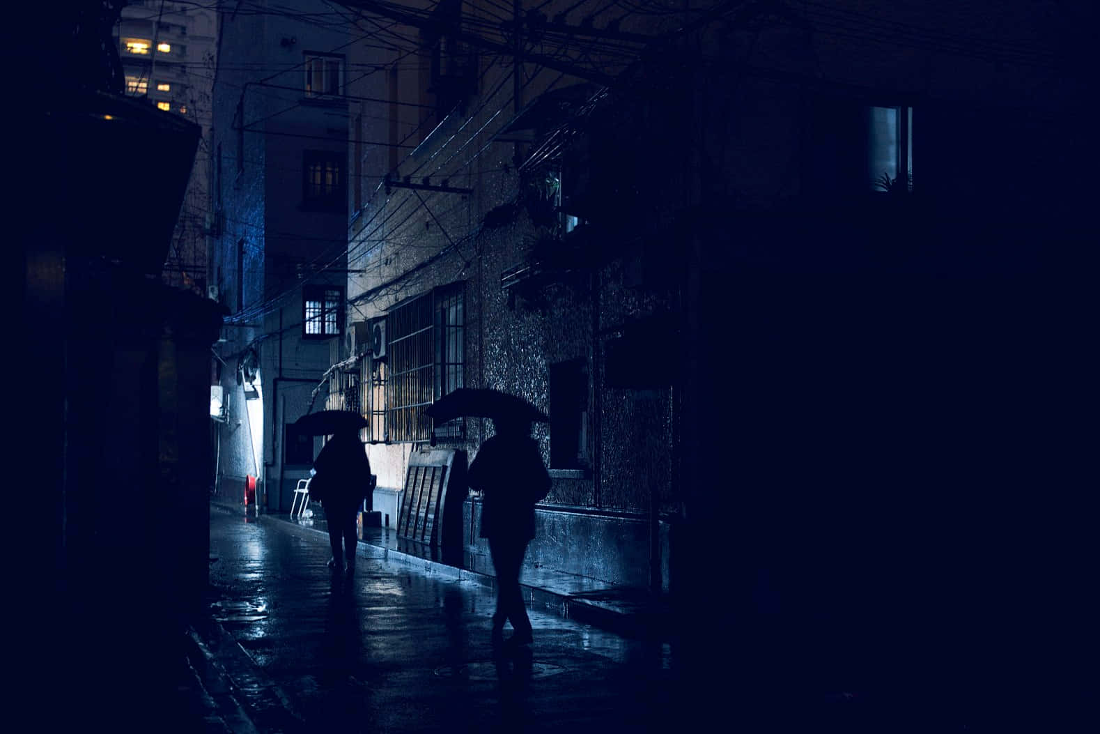神秘 桌布 壁紙 — 兩個撐著雨傘的剪影人物在夜晚昏暗的藍色街燈下沿著濕滑的雨巷行走。