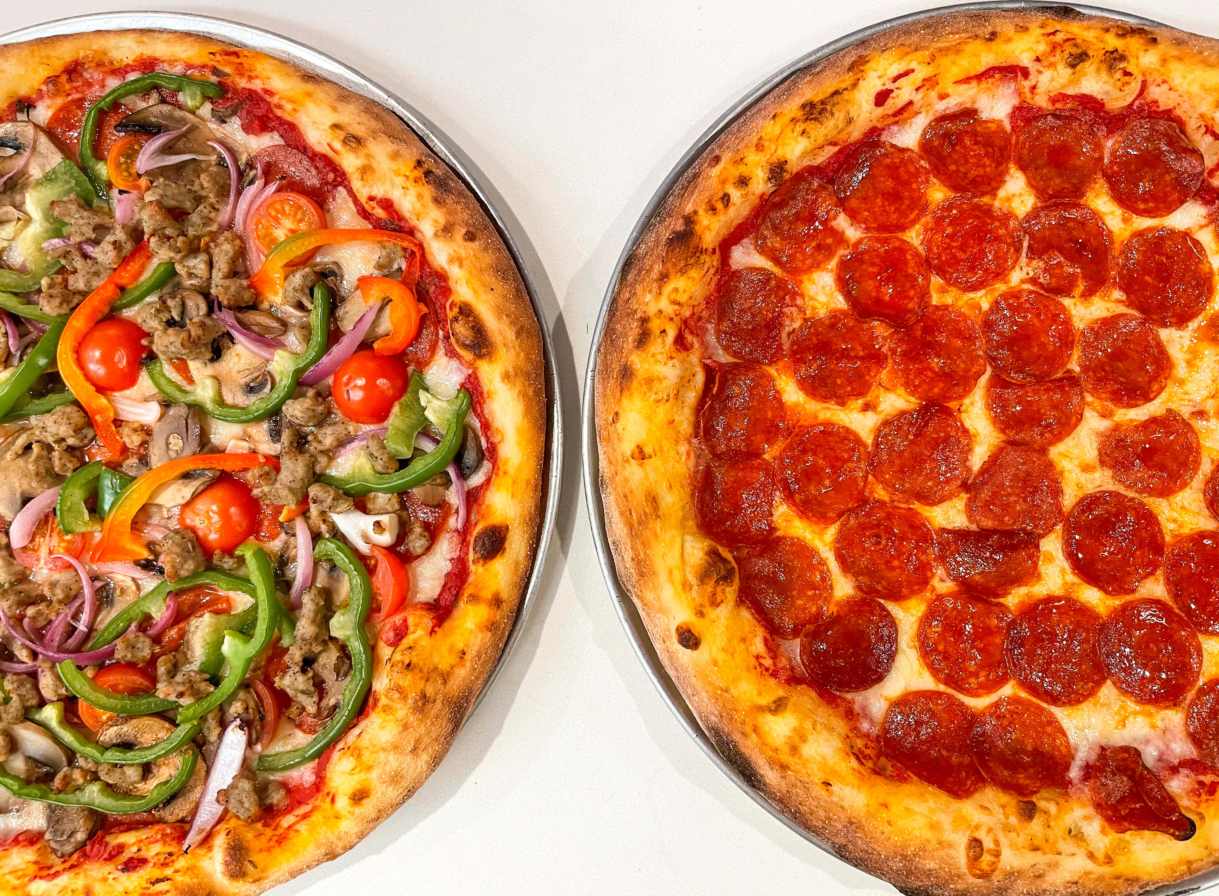Pizza 桌布 壁紙 — 兩個新鮮出爐的披薩，一個裝滿蔬菜和肉，另一個經典義大利辣香腸，並排放在金屬托盤上。