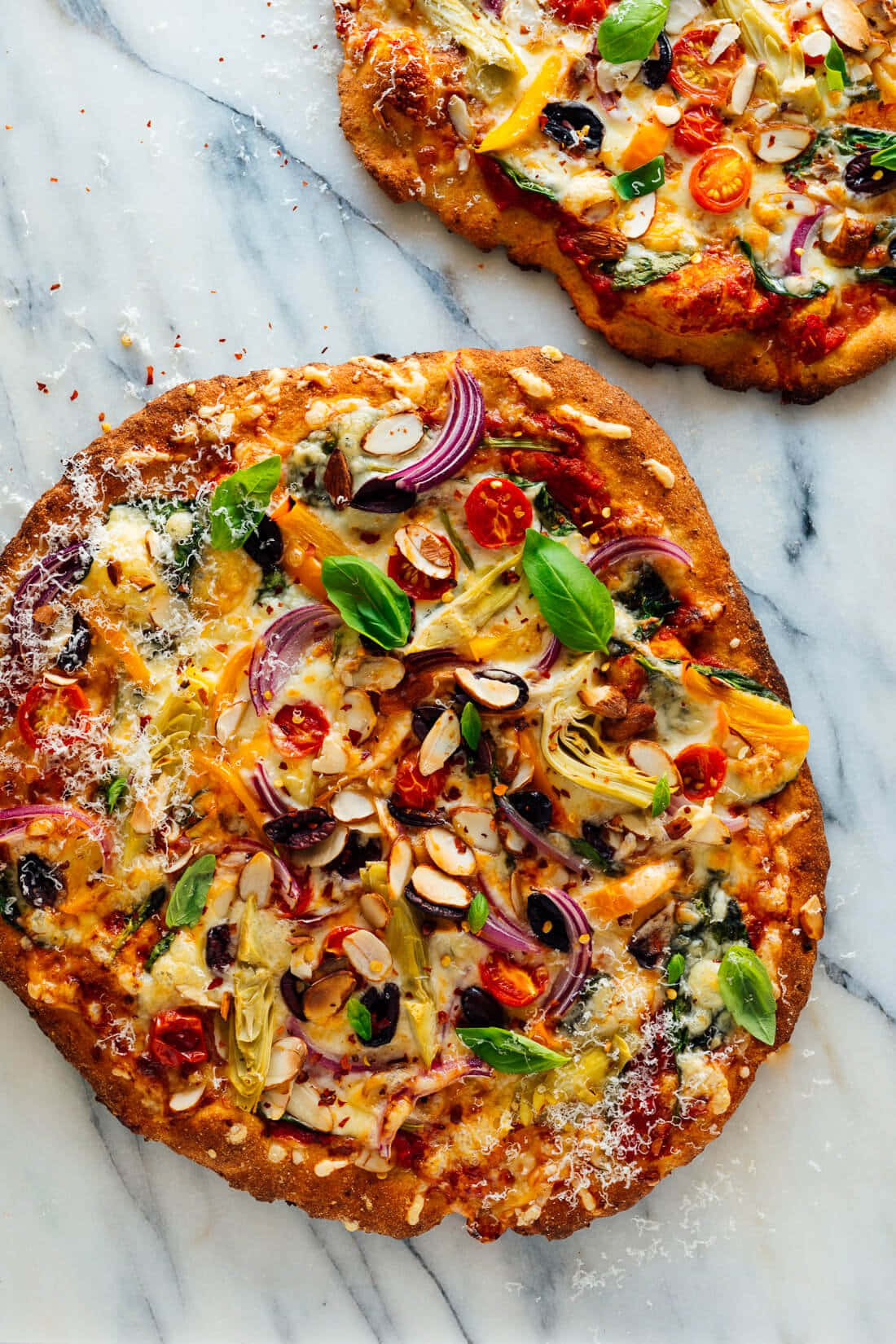Pizza 桌布 壁紙 — 兩個新鮮出爐的蔬菜披薩，上面放有羅勒杏仁和紅洋蔥，放在白色大理石表面上。