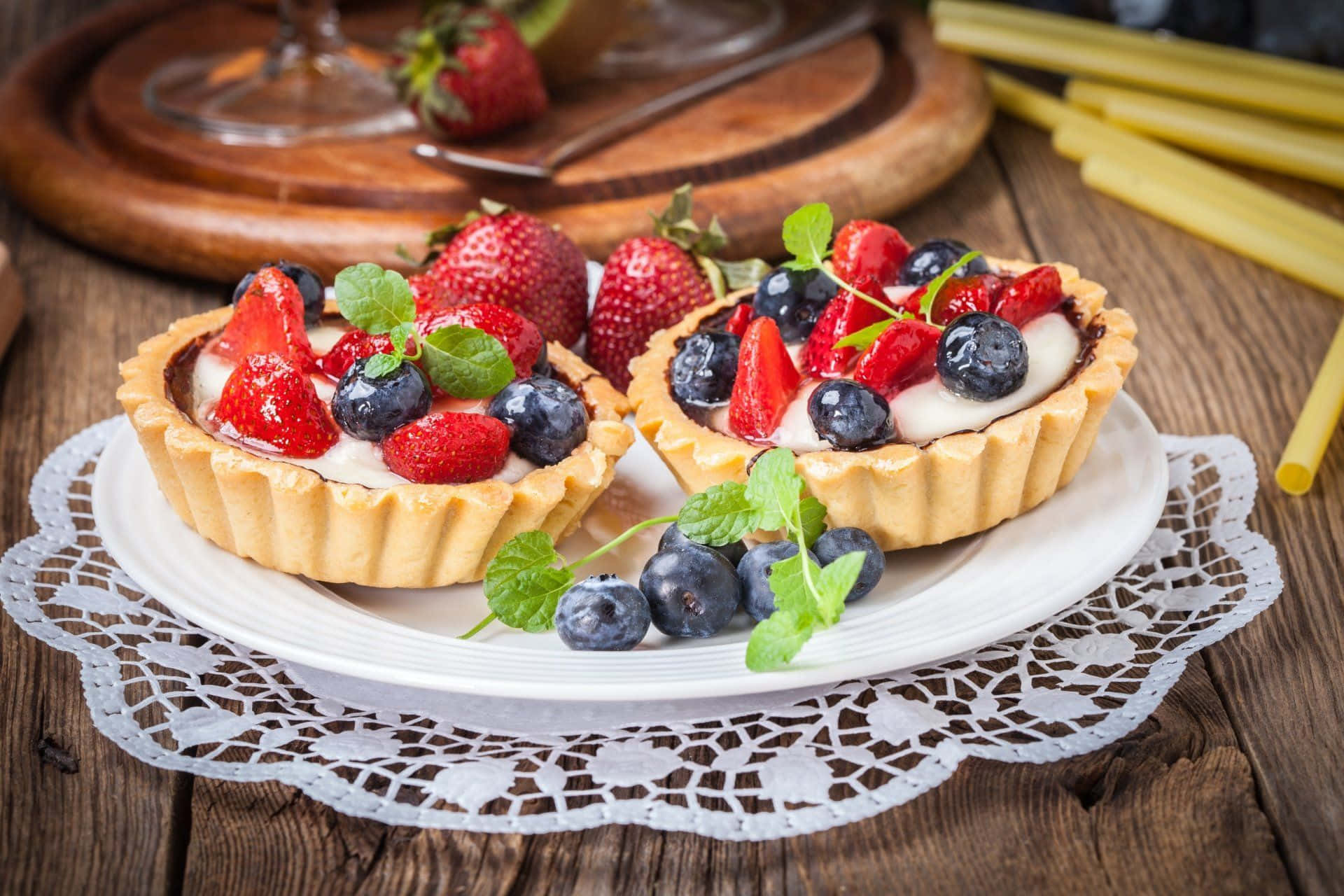 Pastry 桌布 壁紙 — 兩個新鮮莓果塔，上面鋪滿草莓、藍莓和薄荷，放在鄉村木桌上的蕾絲墊上。