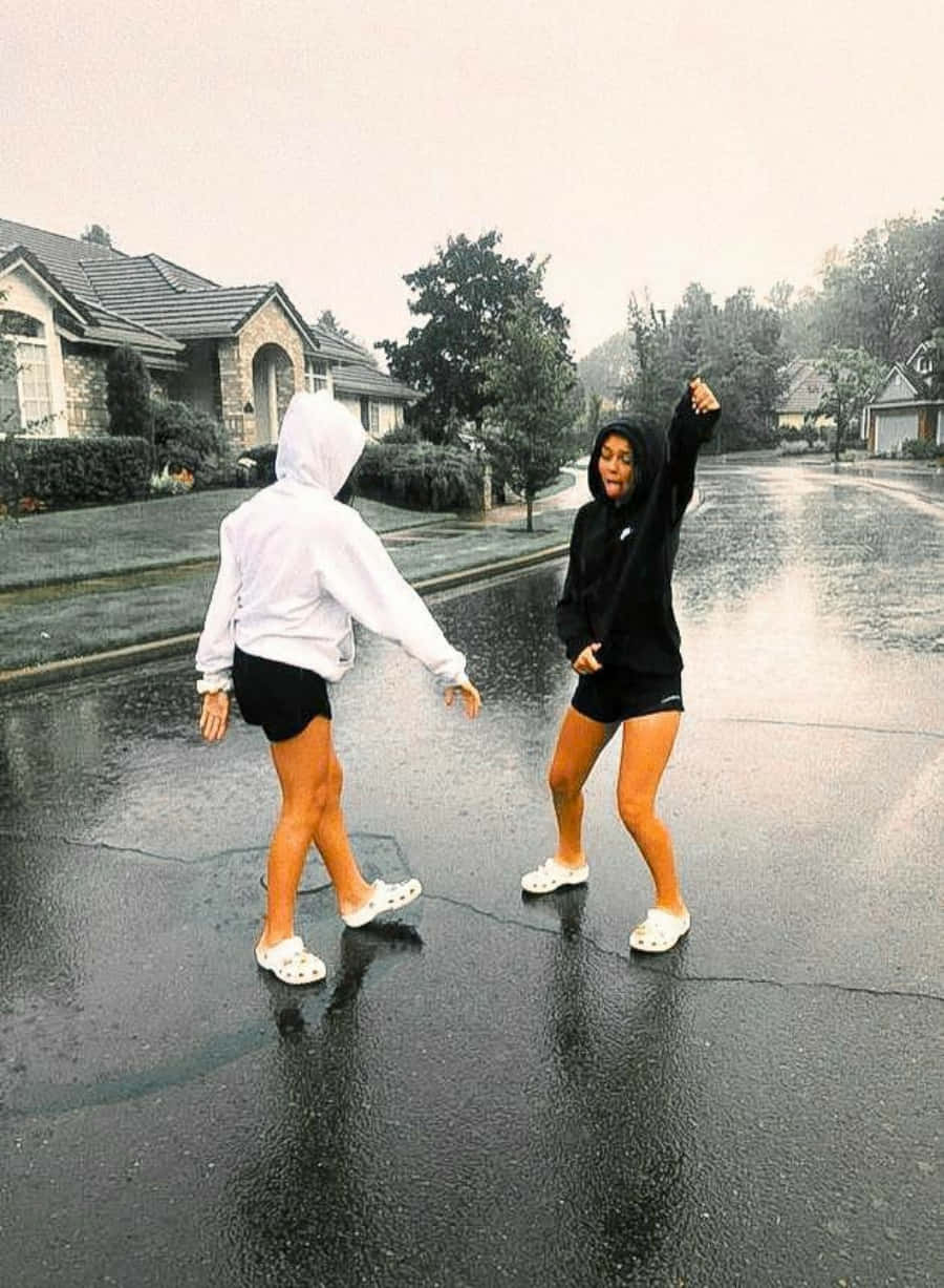 Friends 桌布 壁紙 — 兩個朋友在濕漉漉的郊區街道上快樂地雨中跳舞，笑著在水坑中濺水花。