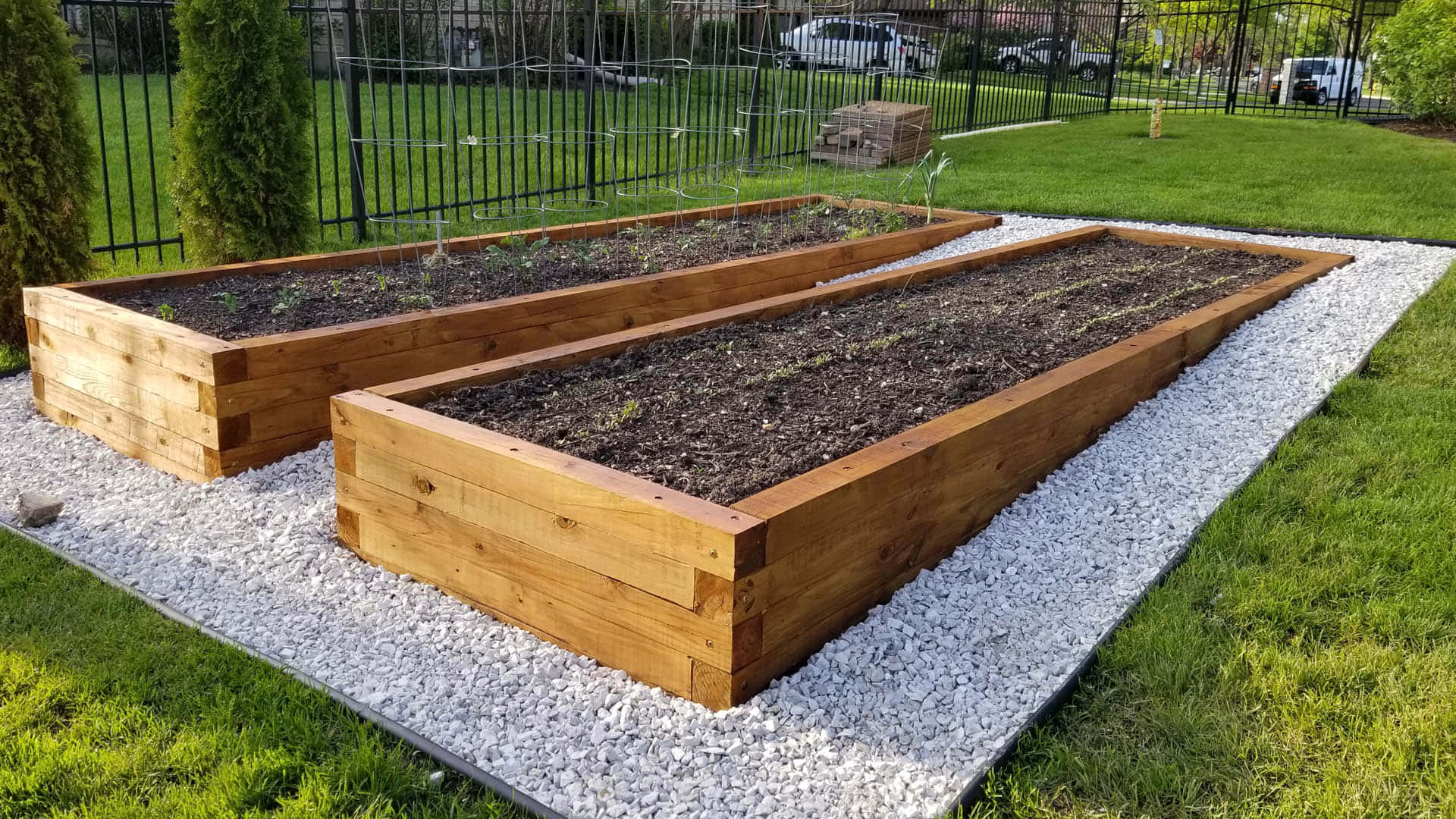 Garden Bed 桌布 壁紙 — 兩個木製高架花床，裝滿泥土和嫩芽，放在陽光充足的後院白色礫石上。