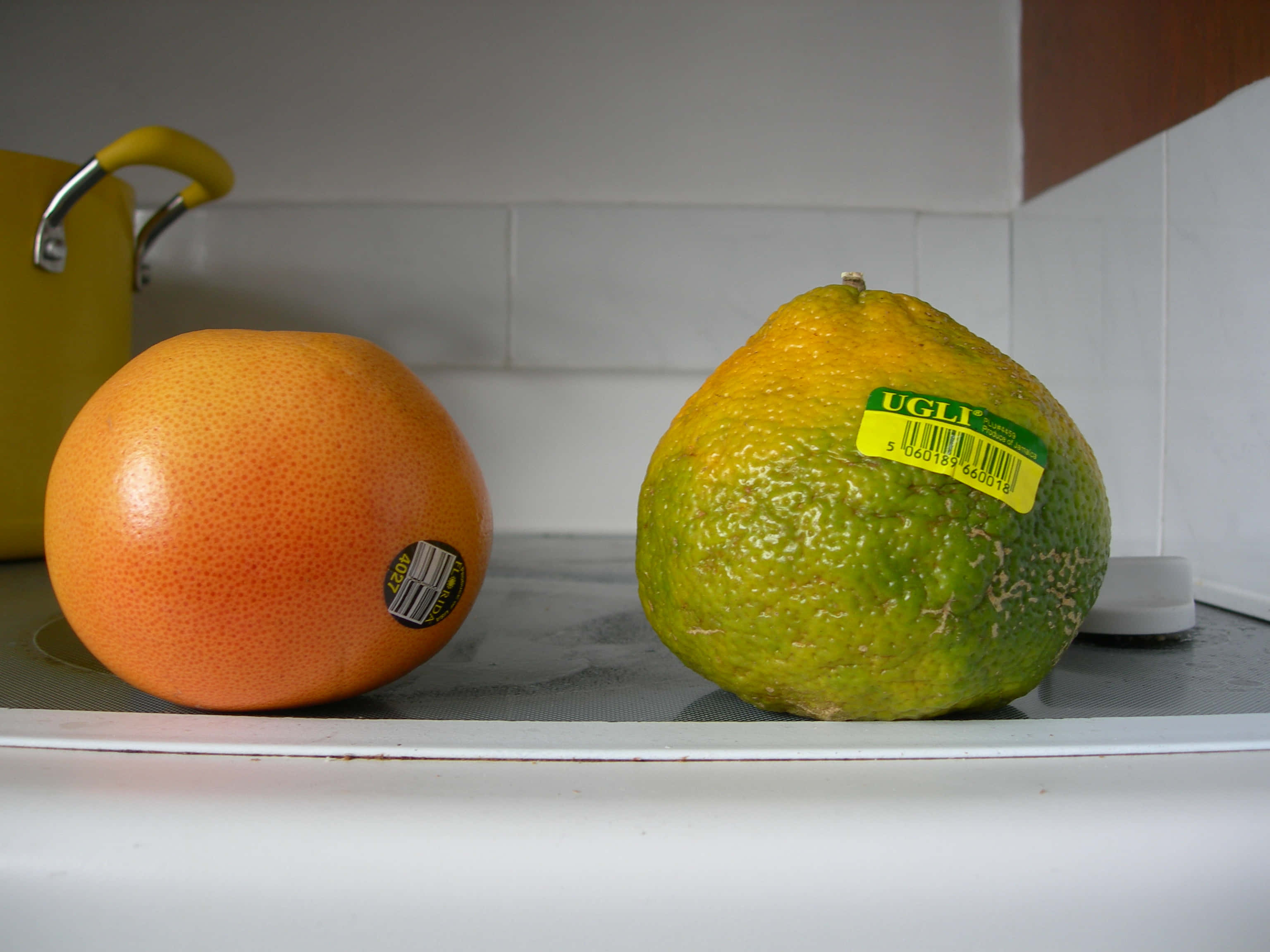 Fruits 桌布 壁紙 — 兩個柑橘類水果一個光滑的橙西柚和一個凹凸不平的黃綠色柑橘並排放在廚房檯面上。
