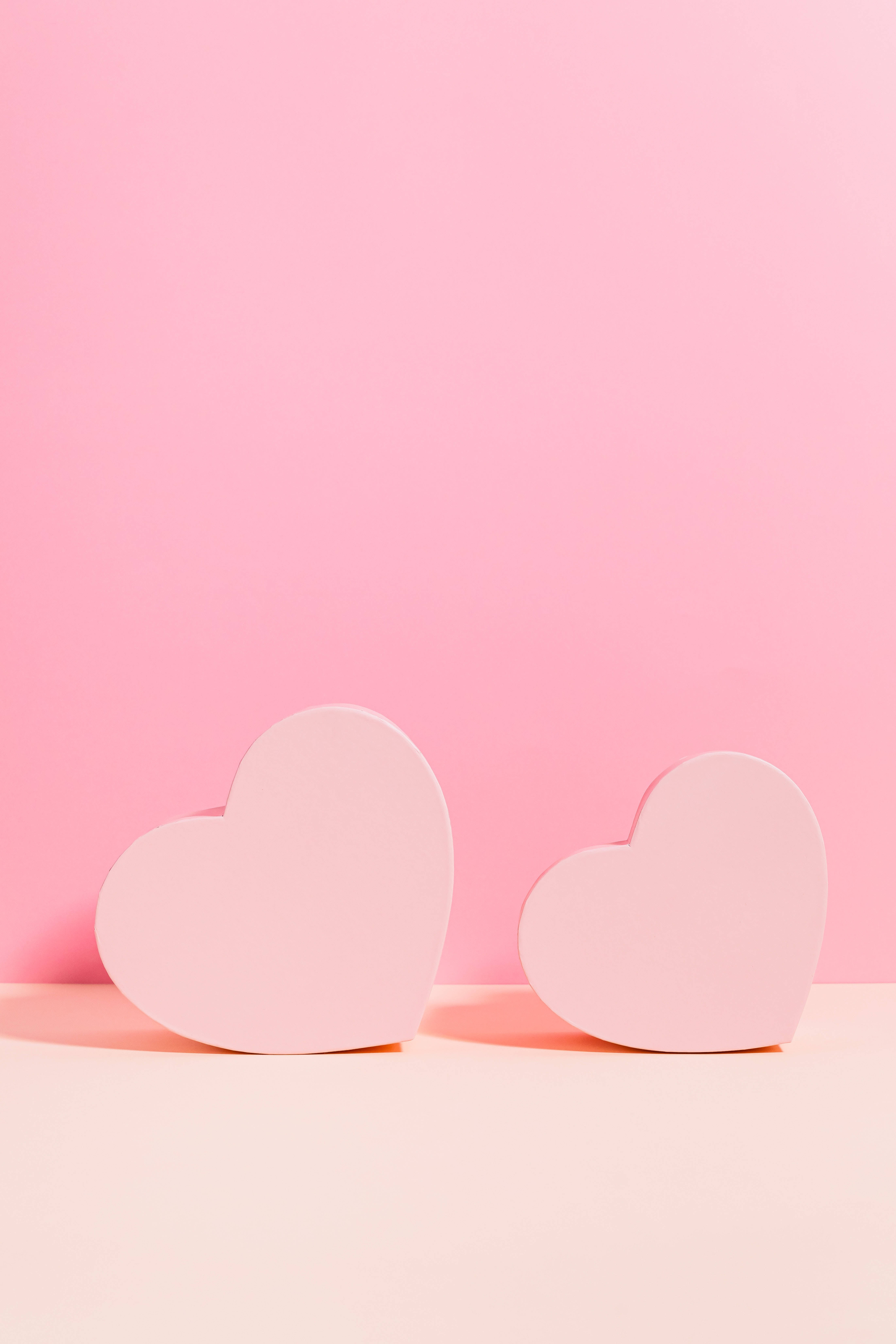 Pastel Pink Heart 桌布 壁紙 — 兩個柔軟的粉紅色心形圖案放在淺色表面上，襯托著純色粉彩粉紅色背景。