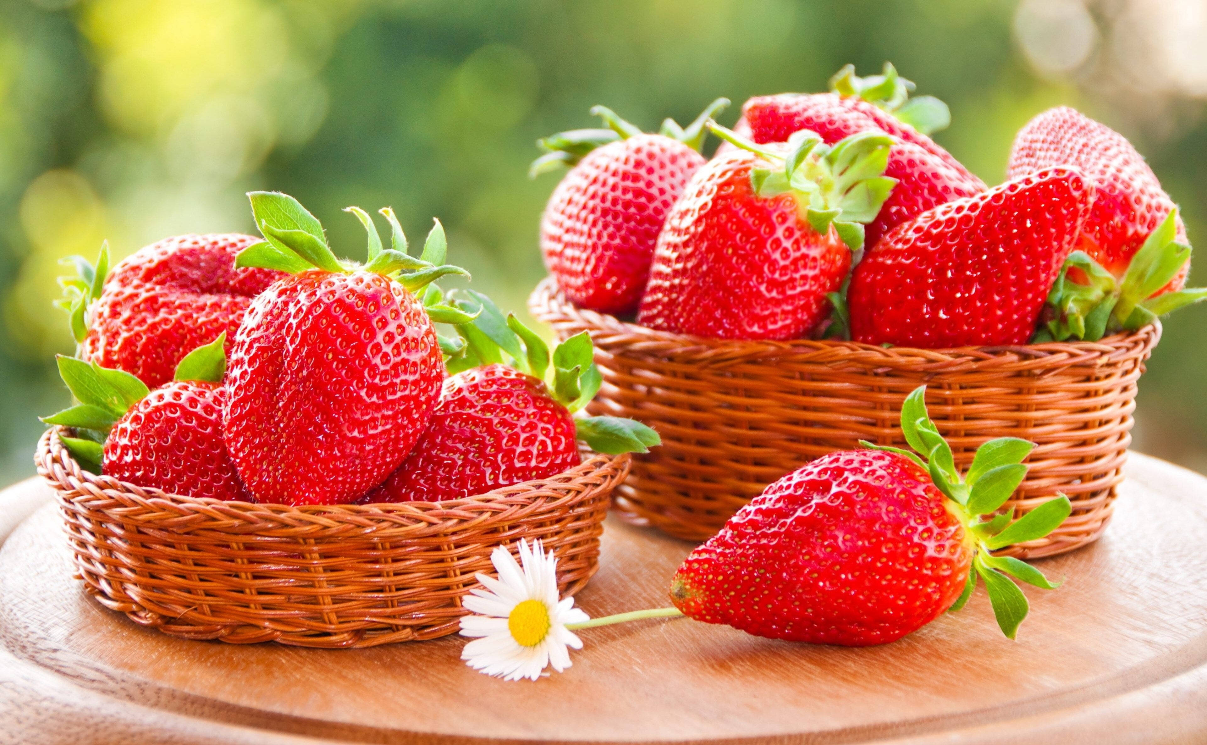 Strawberry 桌布 壁紙 — 兩個柳條籃子裝滿了飽滿的紅色草莓，還有一個放在木桌上的一朵白色雛菊旁邊。