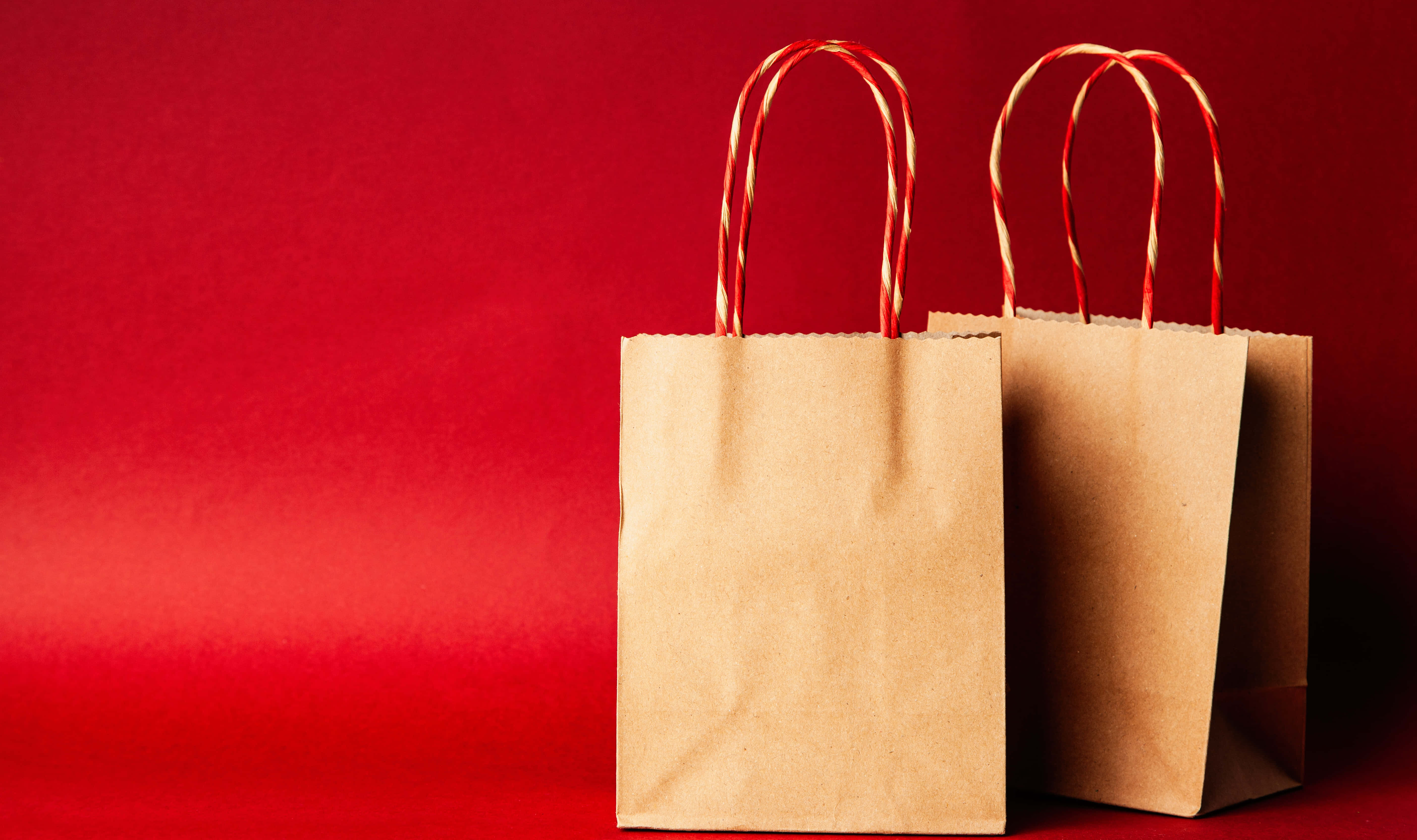 Shopping 桌布 壁紙 — 兩個棕色紙禮品袋，帶有拐杖糖手柄，立在豐富的紅色漸變背景上。