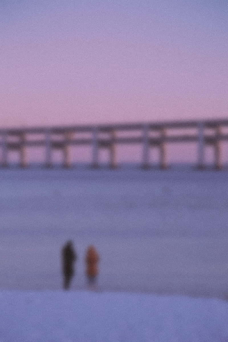 Purple Aesthetic Tumblr 桌布 壁紙 — 兩個模糊的身影在柔和的粉紫色暮色天空下，沿著積雪的碼頭行走。