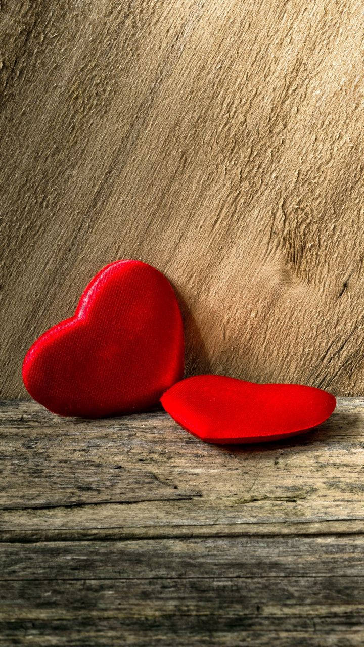 Love Phone 桌布 壁紙 — 兩個毛絨紅色心形放在風化的木板上，背景為有紋理的木材。