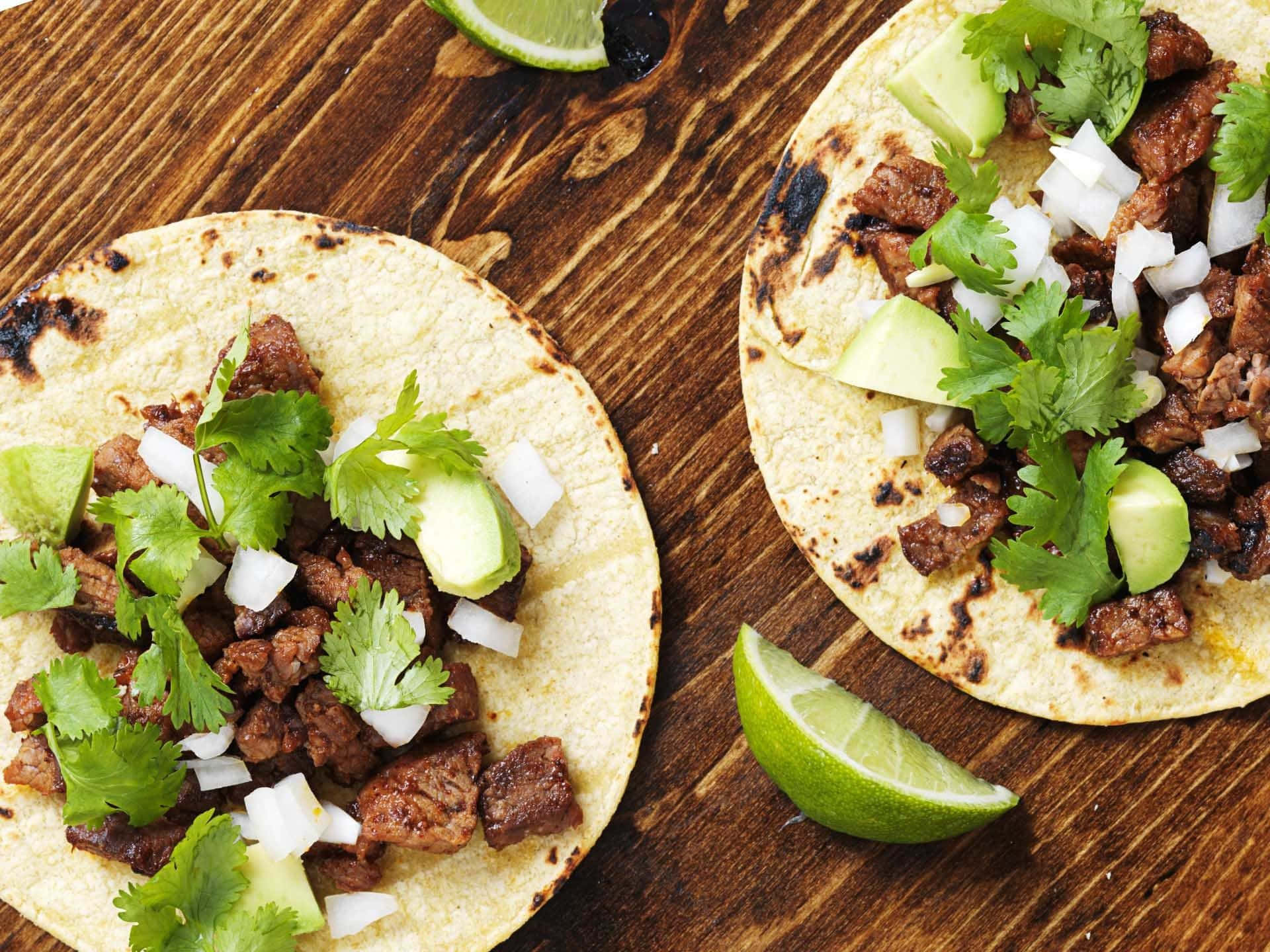 Mexican 桌布 壁紙 — 兩個烤牛肉玉米餅，上面放有香菜、酪梨和洋蔥，放在質樸的木板上，搭配萊姆角。