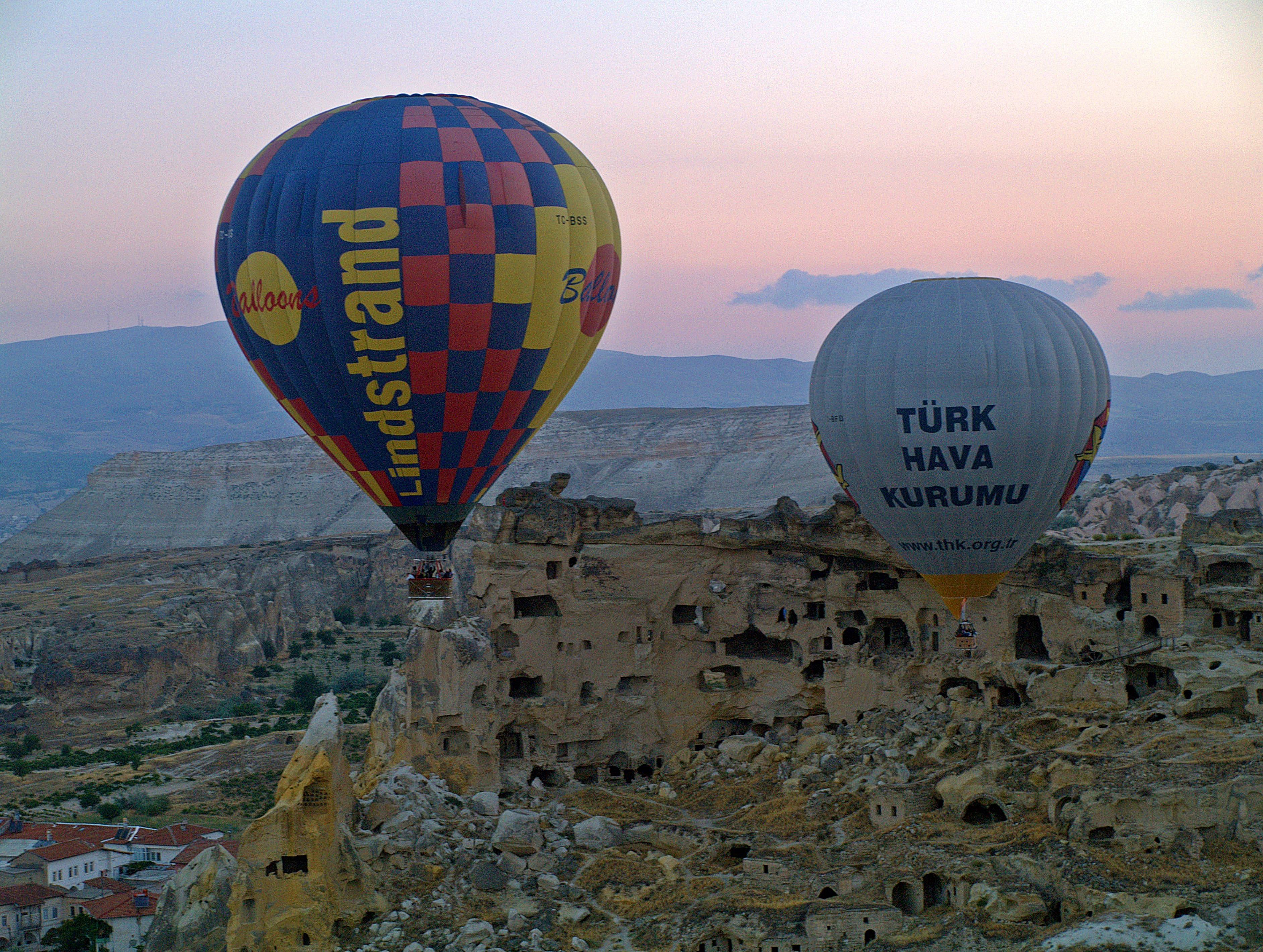 Cappadocia 桌布 壁紙 — 兩個熱氣球在卡帕多奇亞的暮色中飄過古老的洞穴住所。