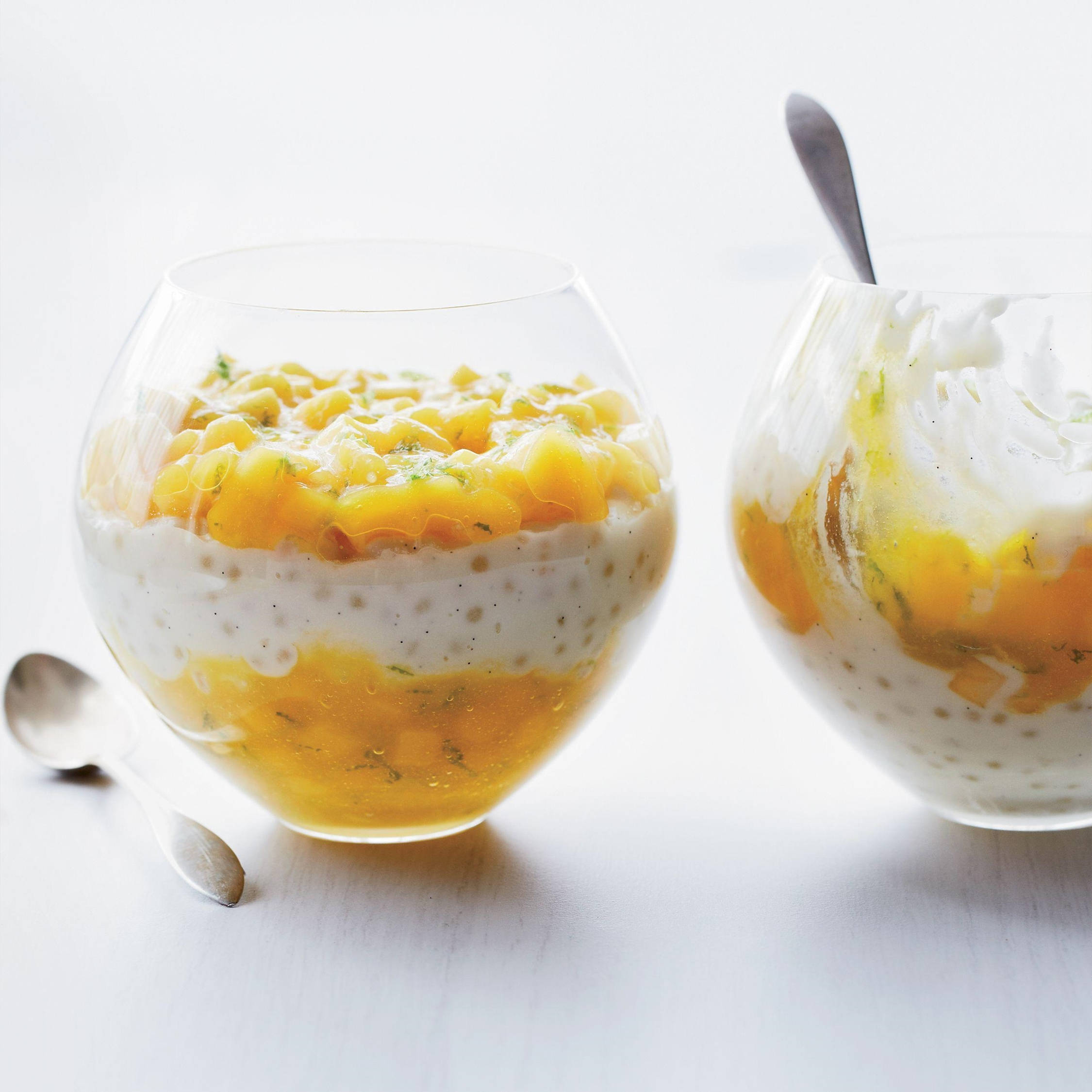Mango 桌布 壁紙 — 兩個玻璃碗盛裝著奶油芒果西米露甜品，上面放上新鮮芒果丁和薄荷葉，置於亮白色表面上。