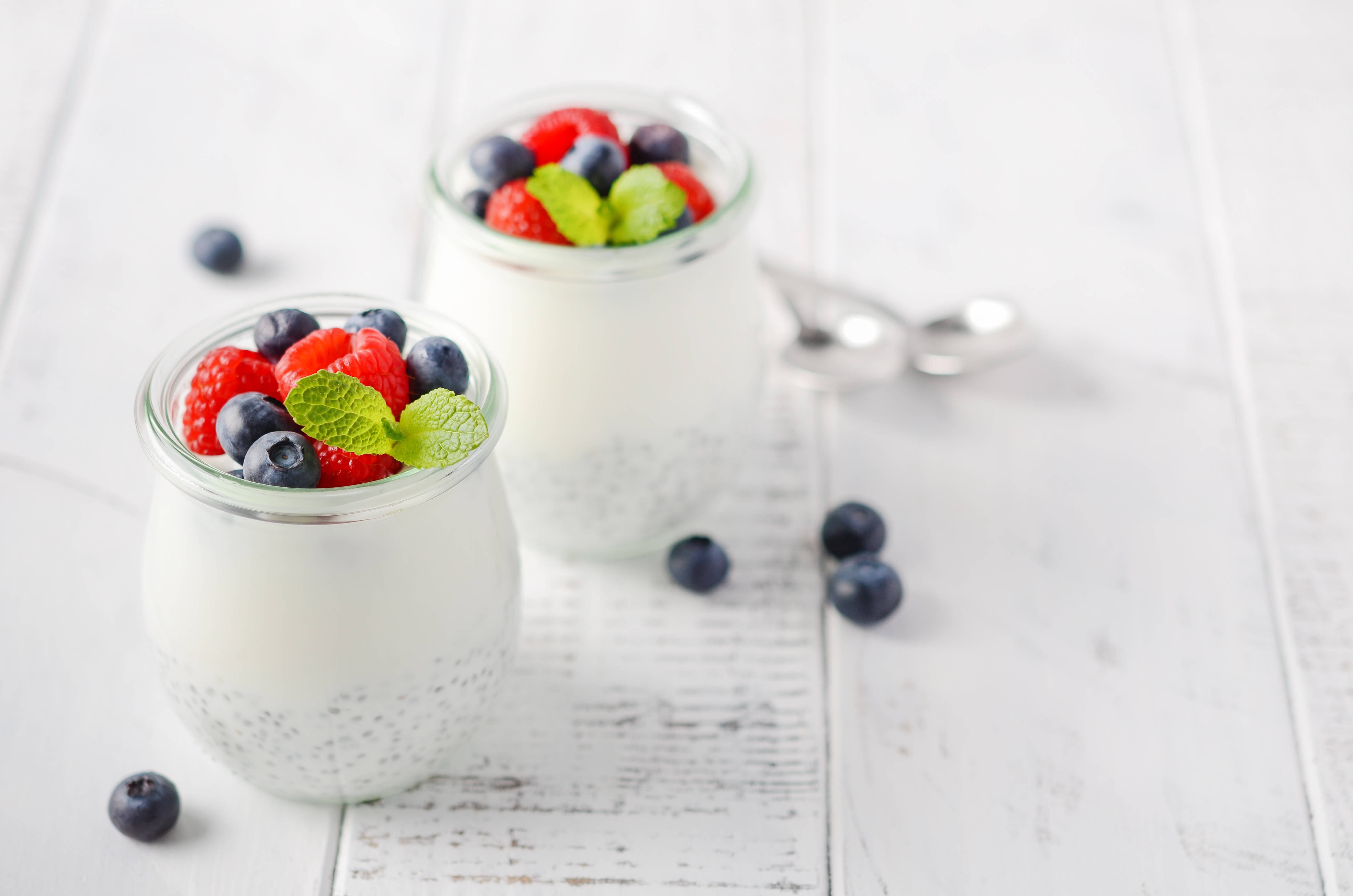 Berry 桌布 壁紙 — 兩個玻璃罐裝滿了奶油奇亞籽布丁，上面放上新鮮莓果和薄荷葉，放在白色木質表面上。