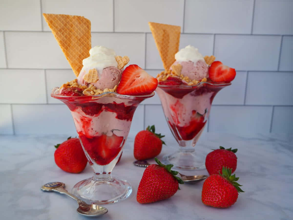 Strawberries 桌布 壁紙 — 兩個玻璃聖代杯，裝滿草莓冰淇淋和新鮮草莓，上面放有鬆餅筒和碎餅乾。