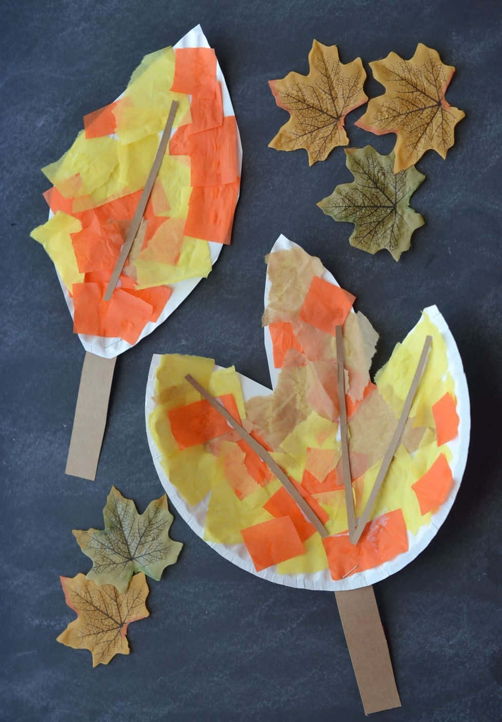 Fall Crafts 桌布 壁紙 — 兩個用紙盤和紙巾製作的手工秋季樹葉工藝品，旁邊放著真正的楓葉，在深灰色表面上。