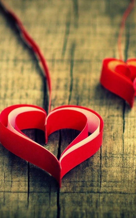 Love Phone 桌布 壁紙 — 兩個由捲曲紙條製成的鮮紅色紙心，放置在經過風化的木質表面上，背景柔和模糊。