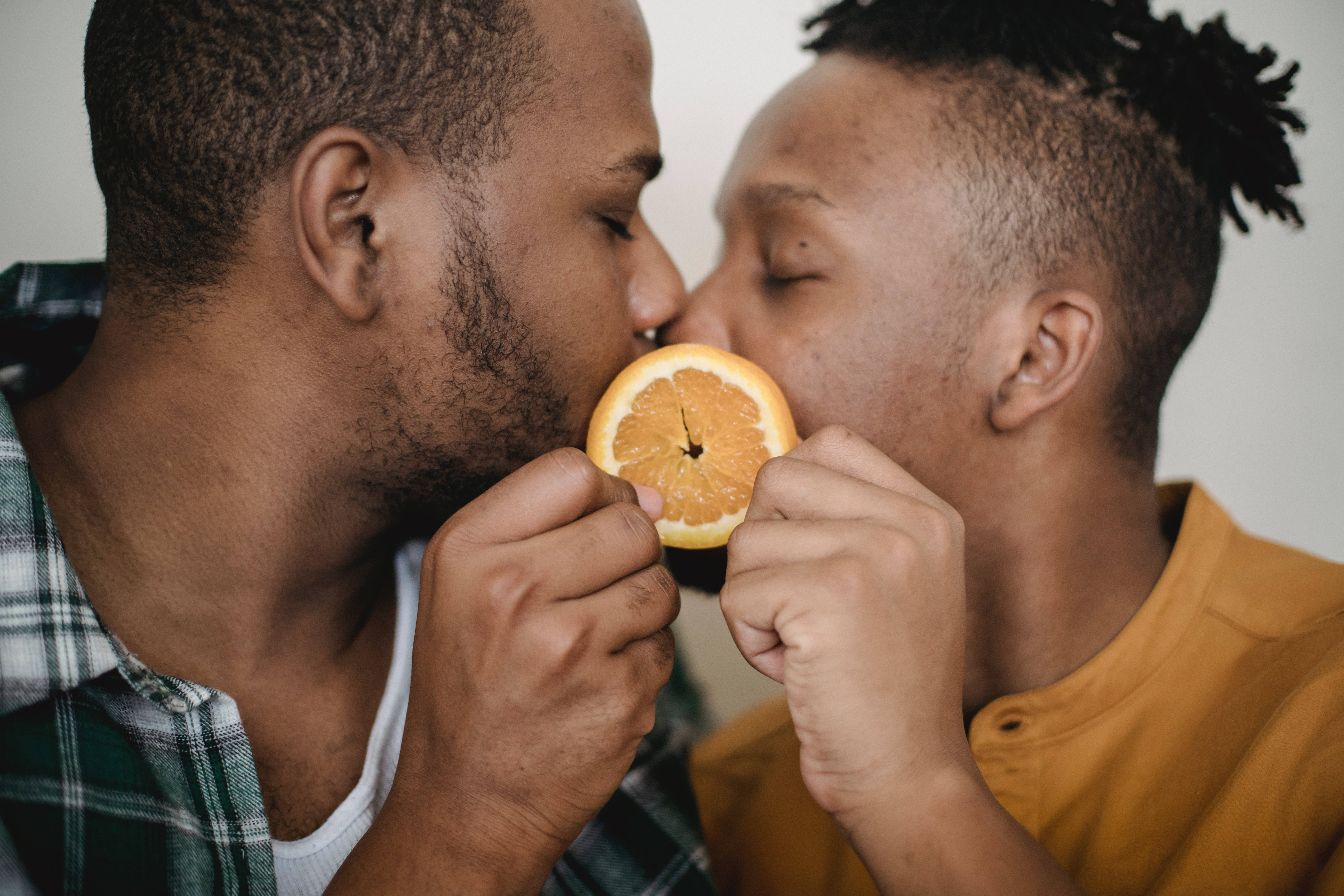 couple kiss 桌布 壁紙 — 兩個男人分享一個俏皮時刻，親吻夾在他們之間的一片柳橙。