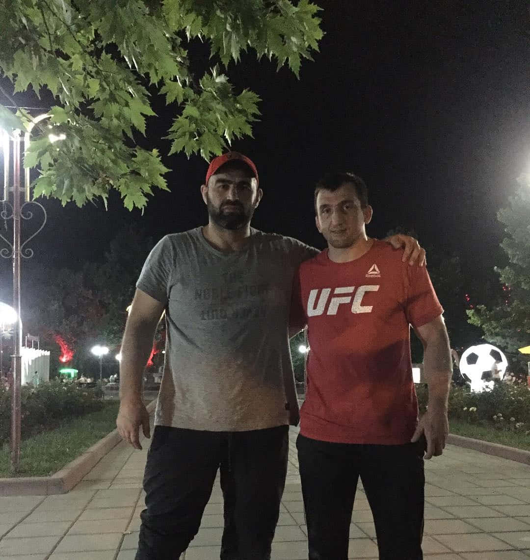 MMA 桌布 壁紙 — 兩個男人在夜晚、發光的街燈下、頭頂有綠色樹葉一起擺姿勢。