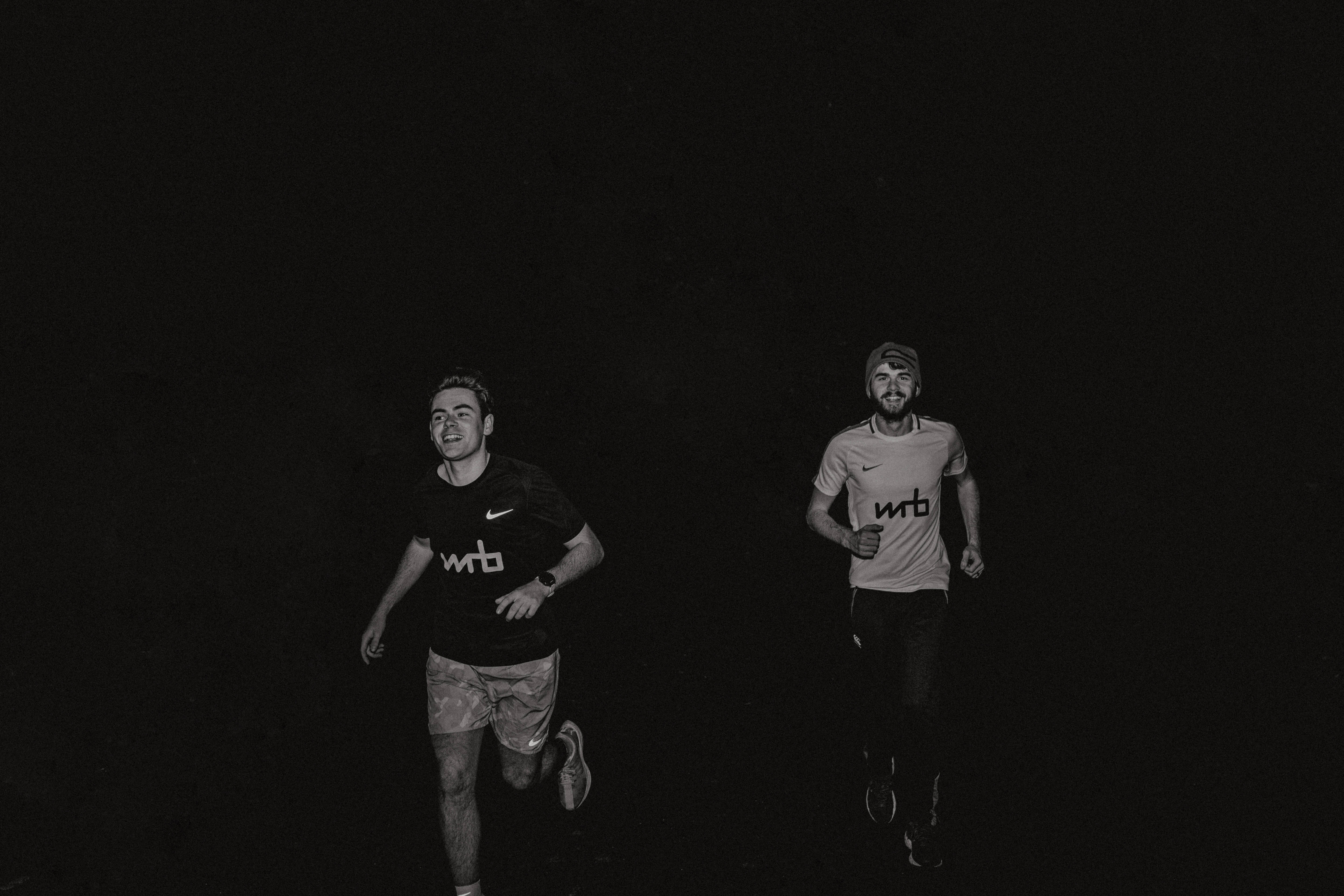 跑步者 桌布 壁紙 — 兩個男人在夜晚慢跑，黑白風格，深色背景，可見運動服裝。