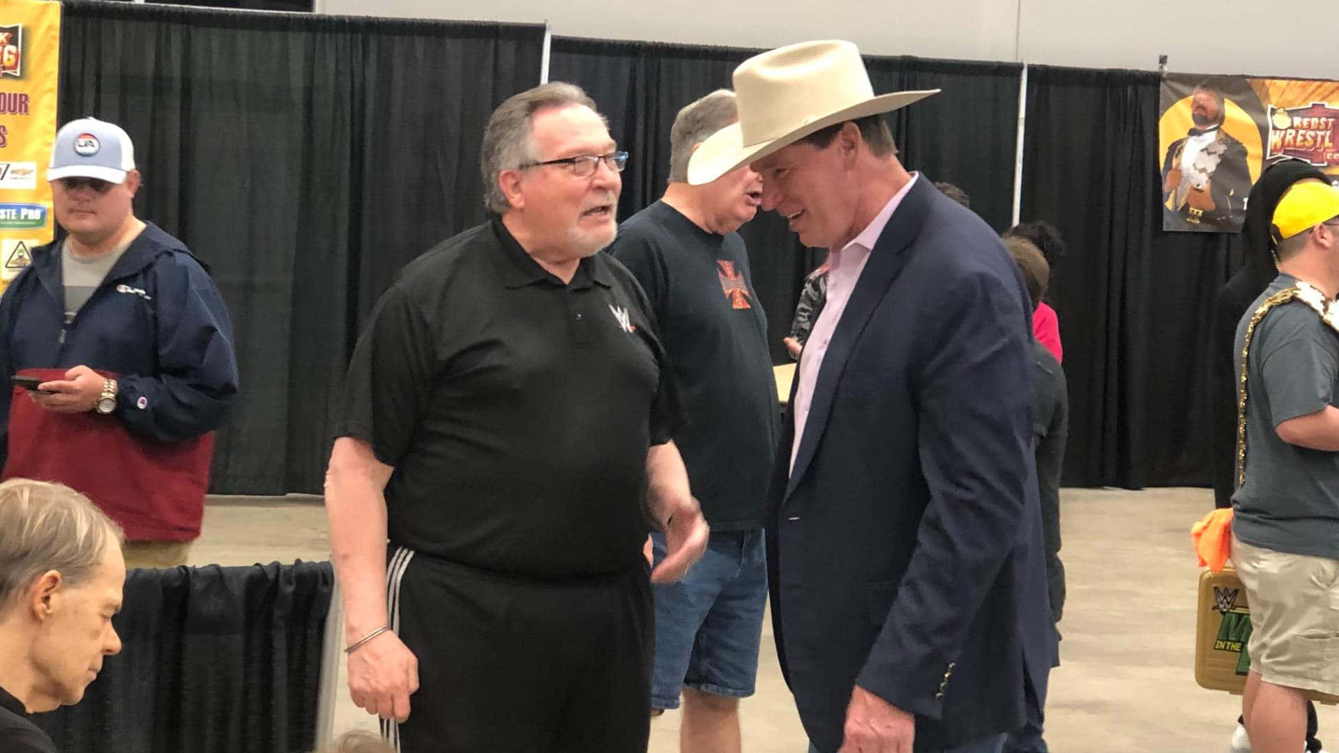 WWE 桌布 壁紙 — 兩個男人在摔角大會上熱情交談，一個戴著牛仔帽，另一個穿著黑色Polo衫。