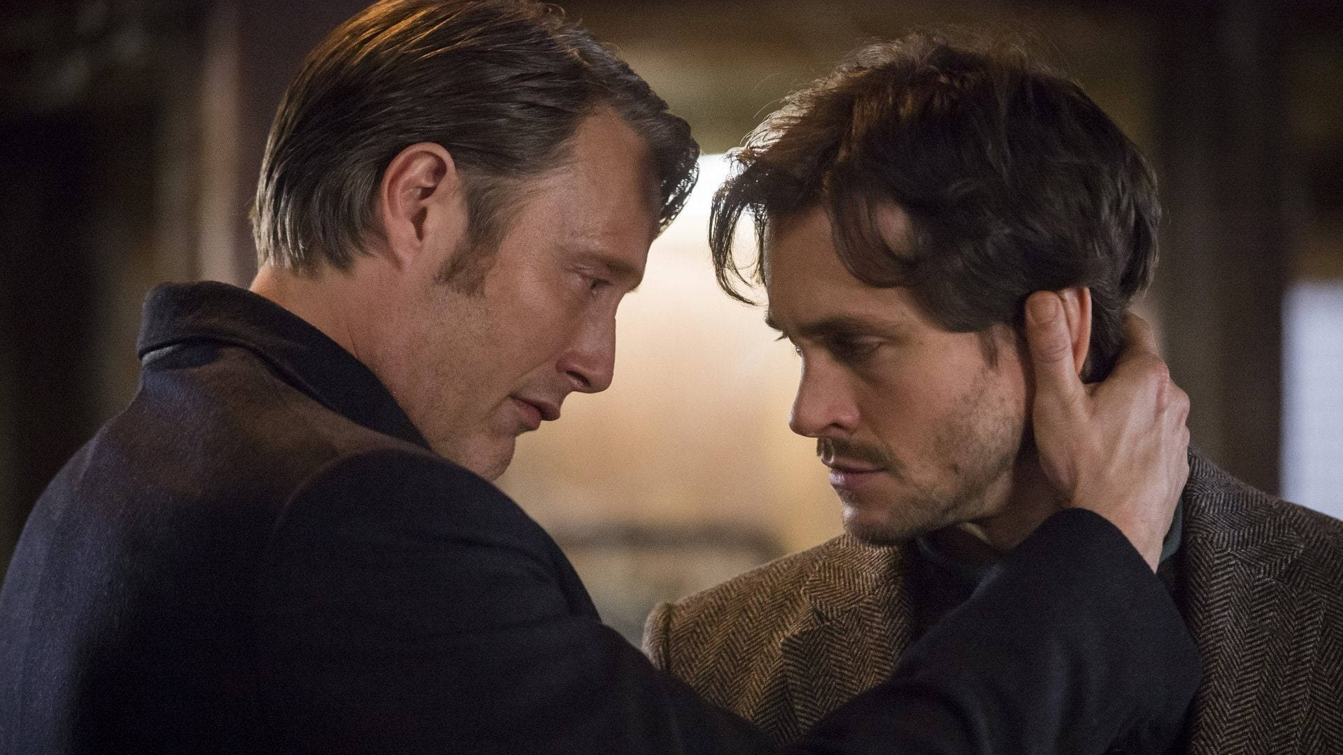 Mads Mikkelsen 桌布 壁紙 — 兩個男人在昏暗的室內環境中近距離分享一個強烈的情感時刻。