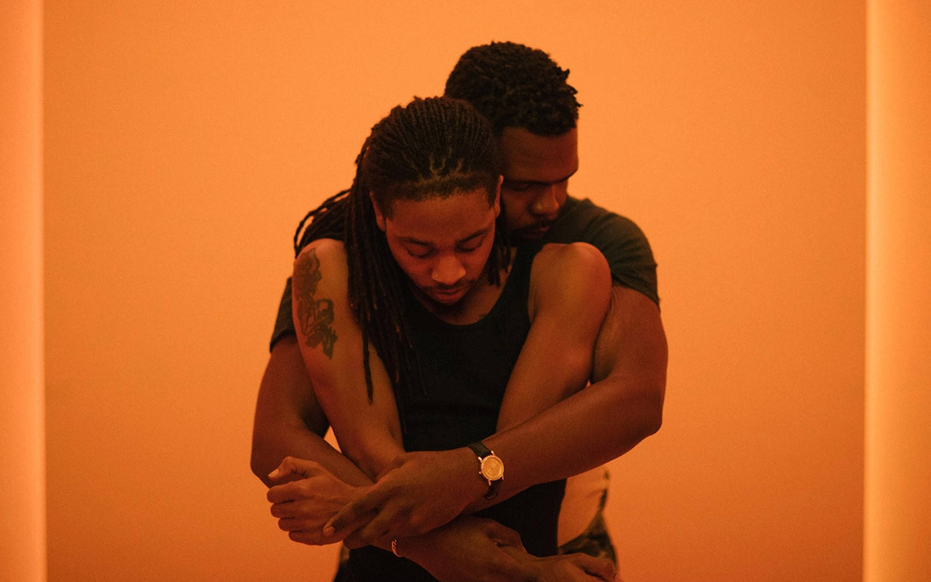 gay hug 桌布 壁紙 — 兩個男人在柔和燈光的橙色房間裡溫暖擁抱，充滿親密與寧靜的聯繫。