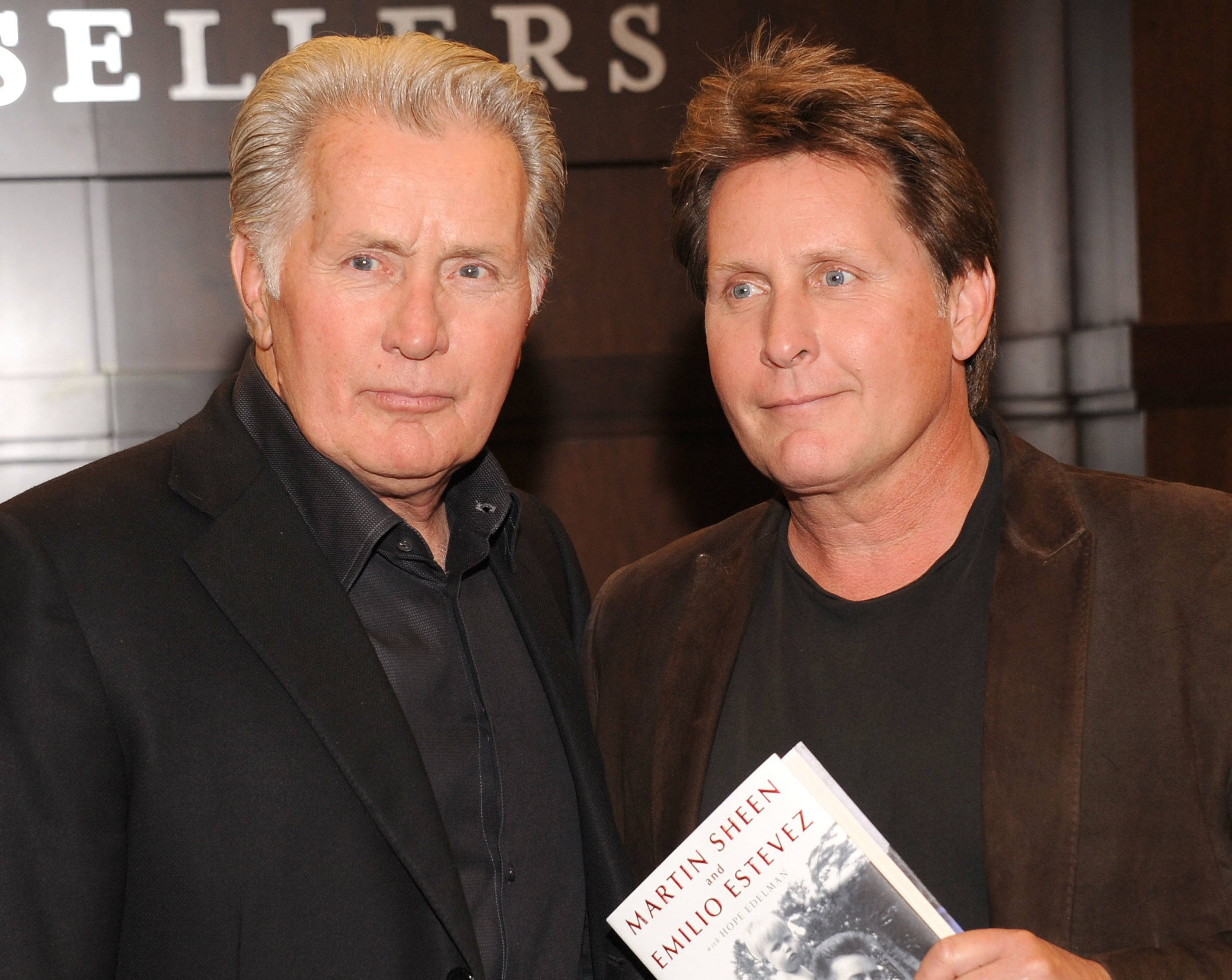 演員 桌布 壁紙 — 兩個男人在活動中並肩而立，其中一人手持一本名為《Martin Sheen and Emilio Estevez》的書。