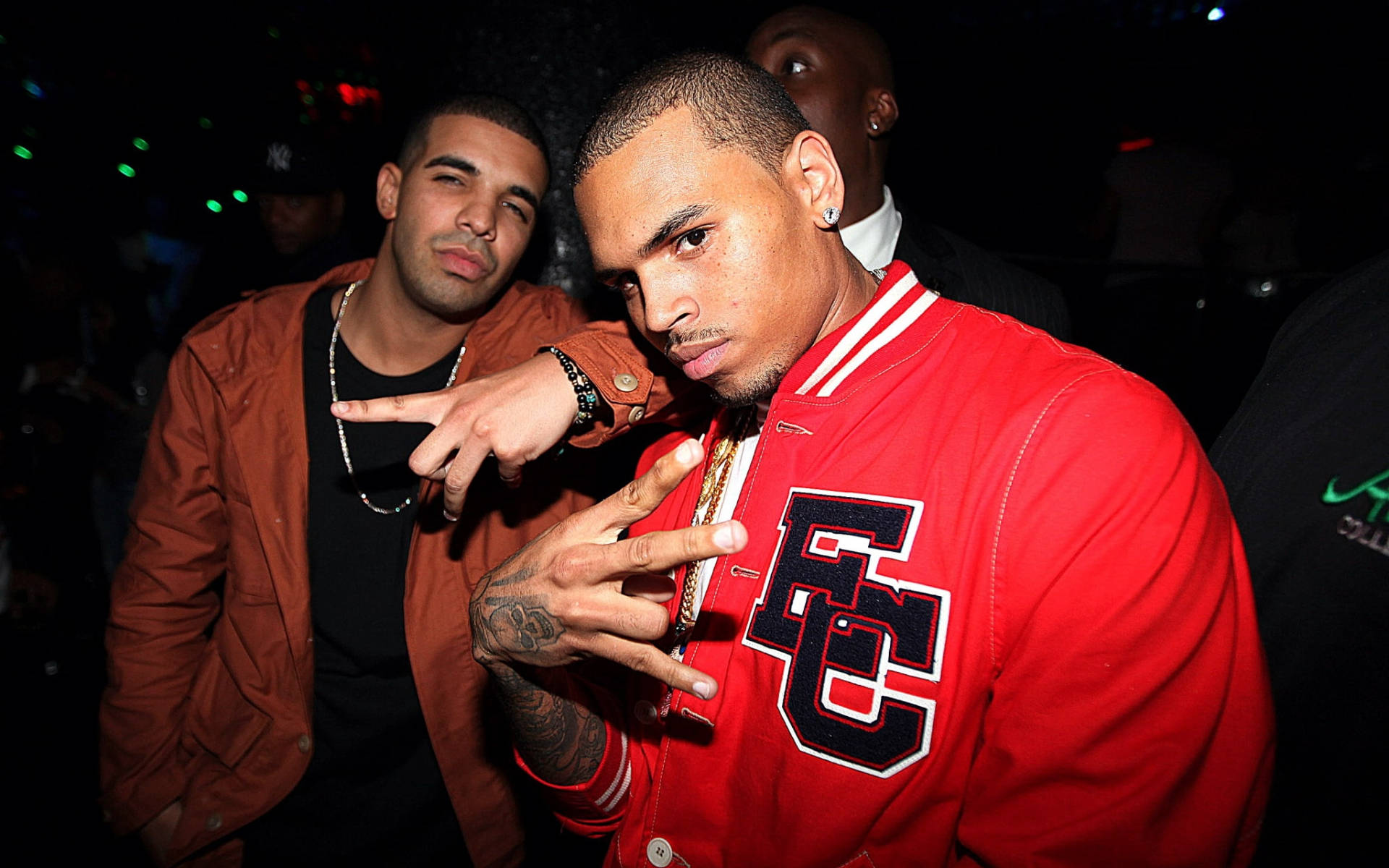 Chris Brown 桌布 壁紙 — 兩個男人在燈光昏暗的俱樂部中自信地擺姿勢，彩色燈光和手臂上的刺青清晰可見。