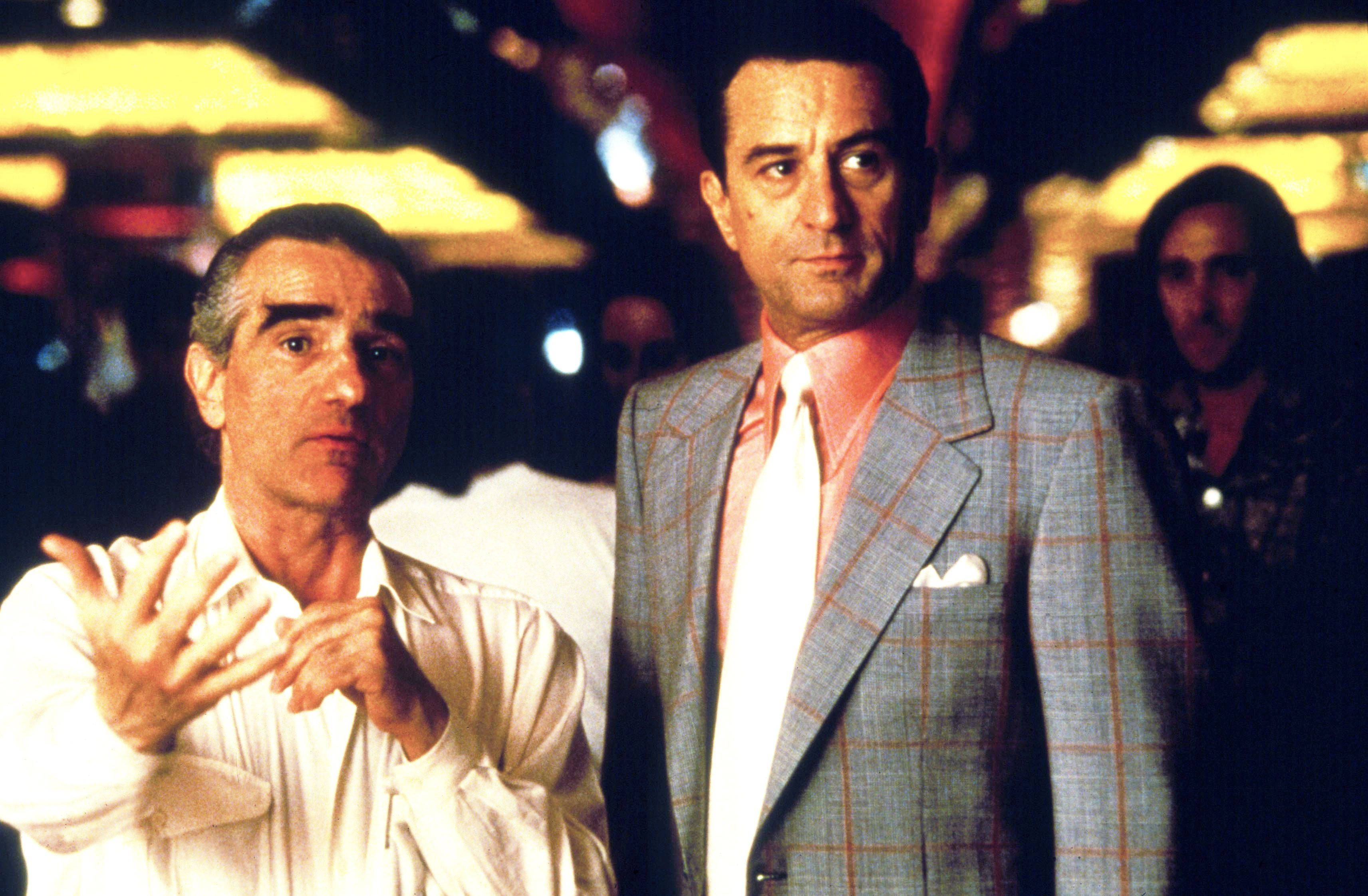 Robert De Niro 桌布 壁紙 — 兩個男人在燈光昏暗的夜總會，一個穿白襯衫做手勢，另一個穿格紋西裝打粉紅色領帶。