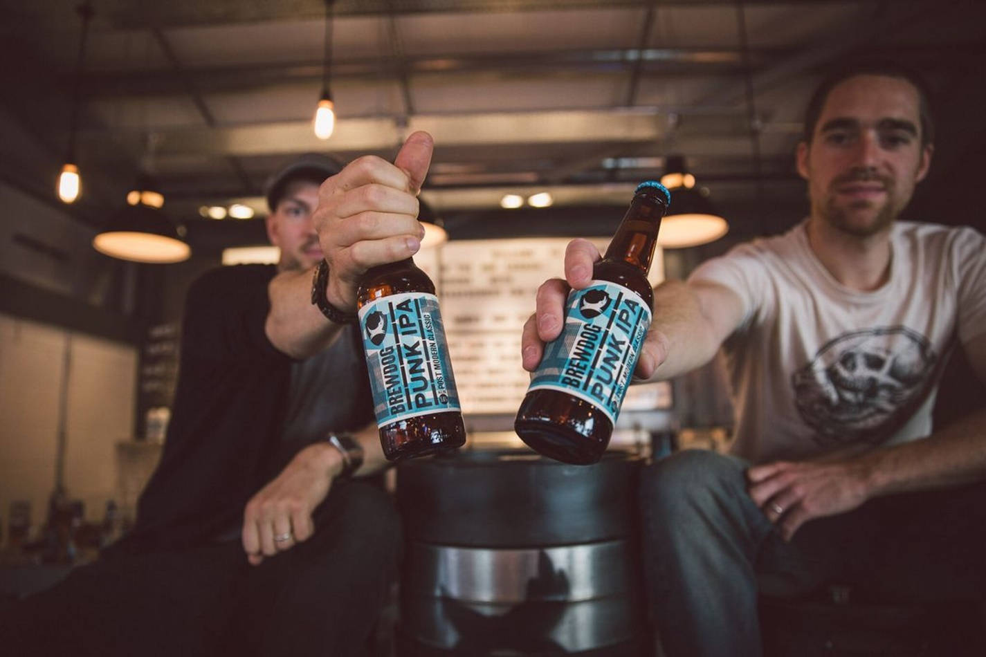 Drink 桌布 壁紙 — 兩個男人在燈光昏暗的酒吧裡碰著BrewDog Punk IPA啤酒瓶，豎起大拇指。