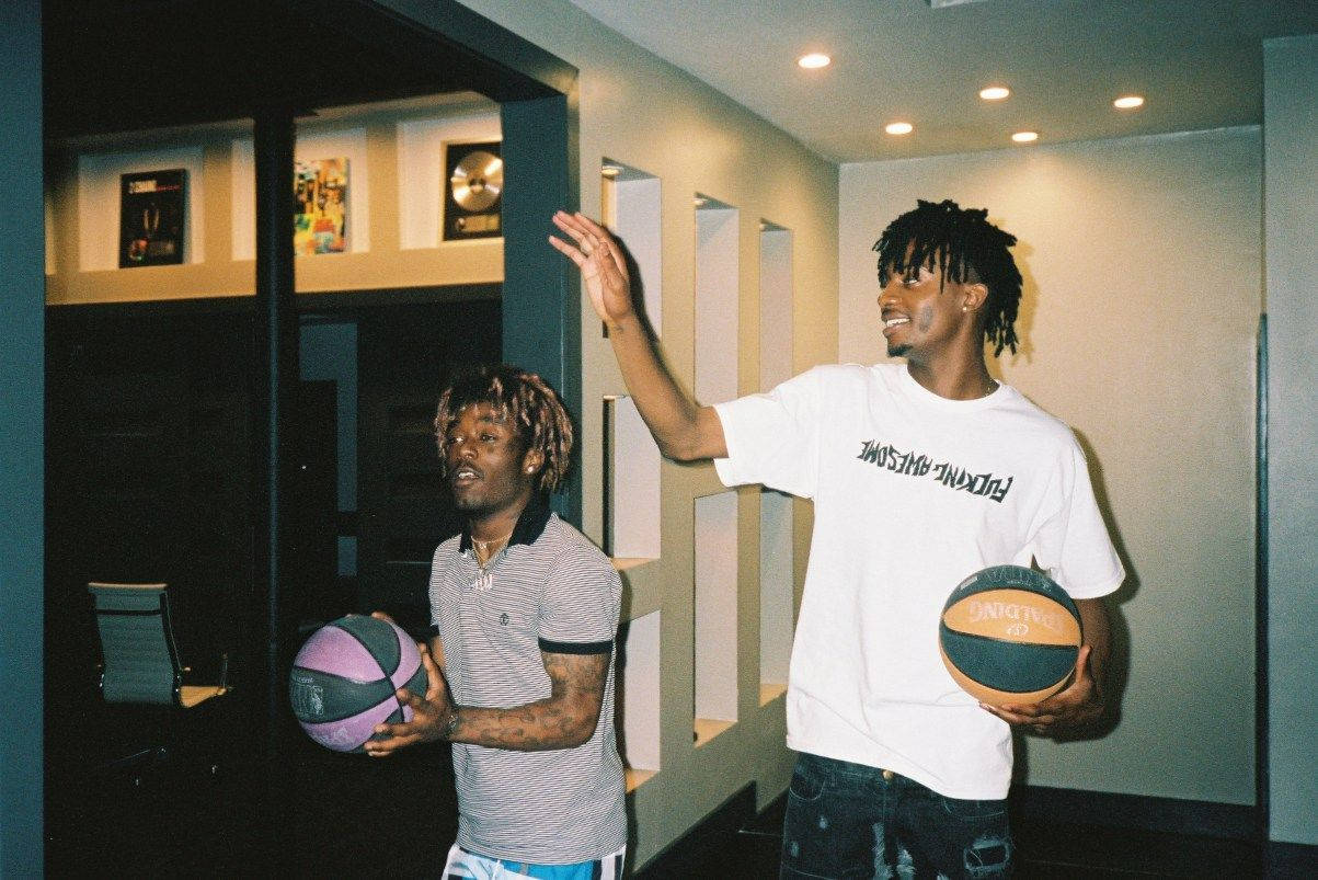 Carti 桌布 壁紙 — 兩個男人在現代走廊裡拿著籃球，一個向上做手勢，另一個看著一個紫色的球。