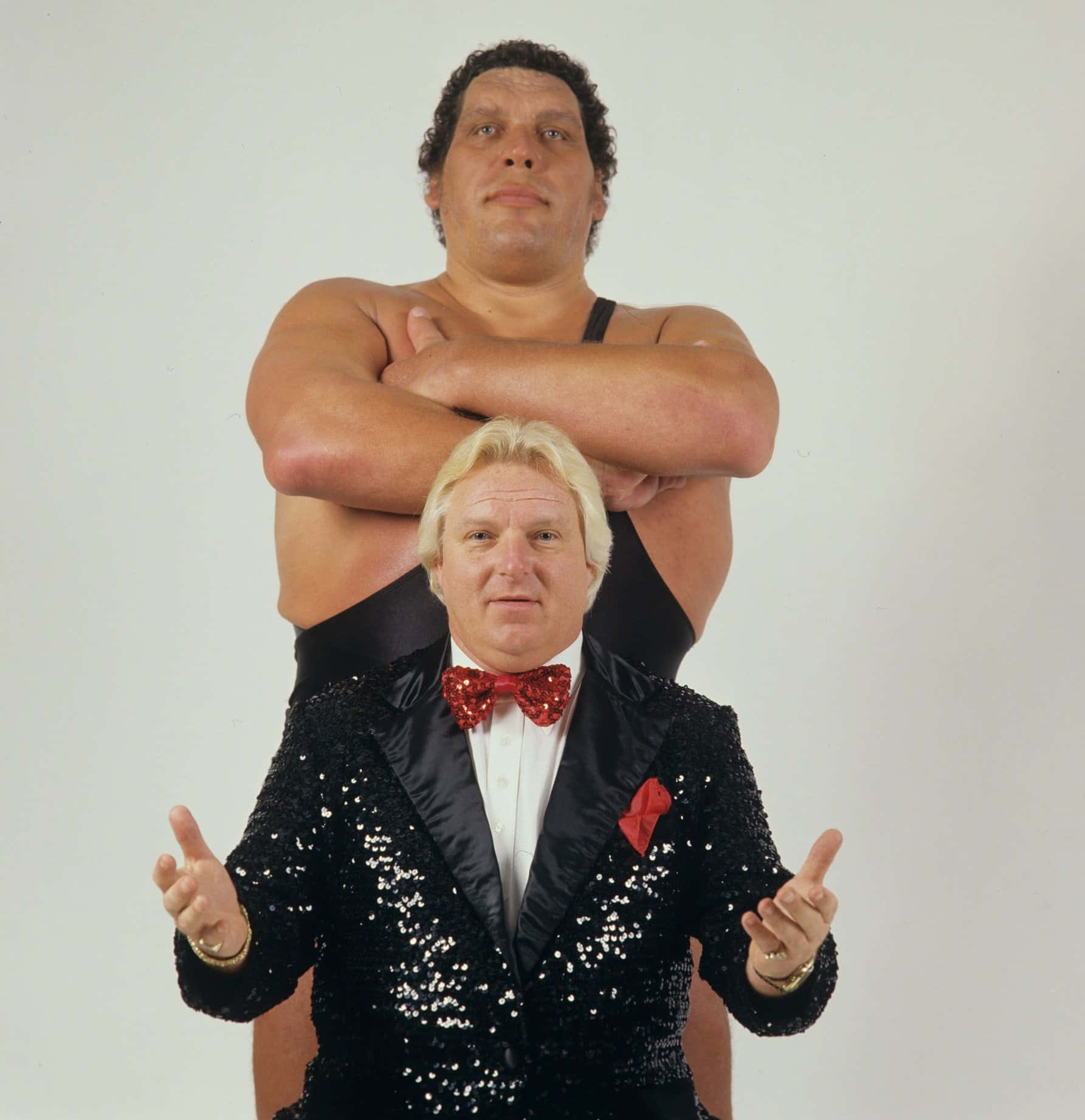 Andre The Giant 桌布 壁紙 — 兩個男人在純白背景前擺姿勢，一個穿著閃亮黑色燕尾服配紅色領結，另一個赤裸上身雙手交叉在背後。